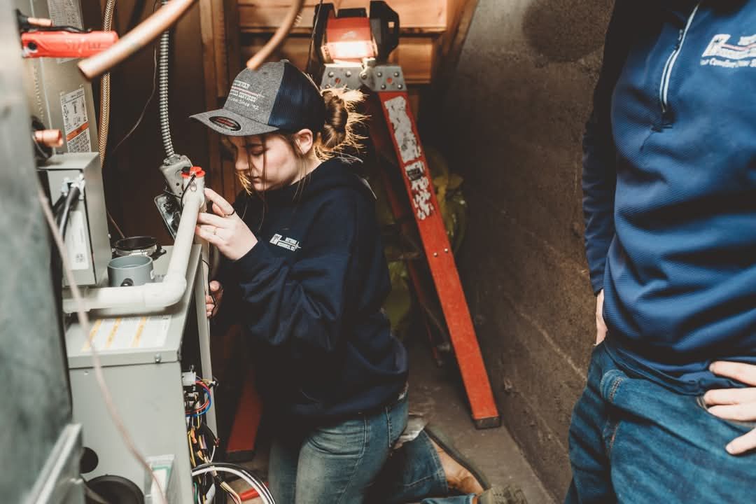 A man and a woman are working on an appliance in a basement.