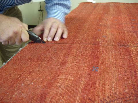 Person using a black utility knife to cut a red fabric on a table.