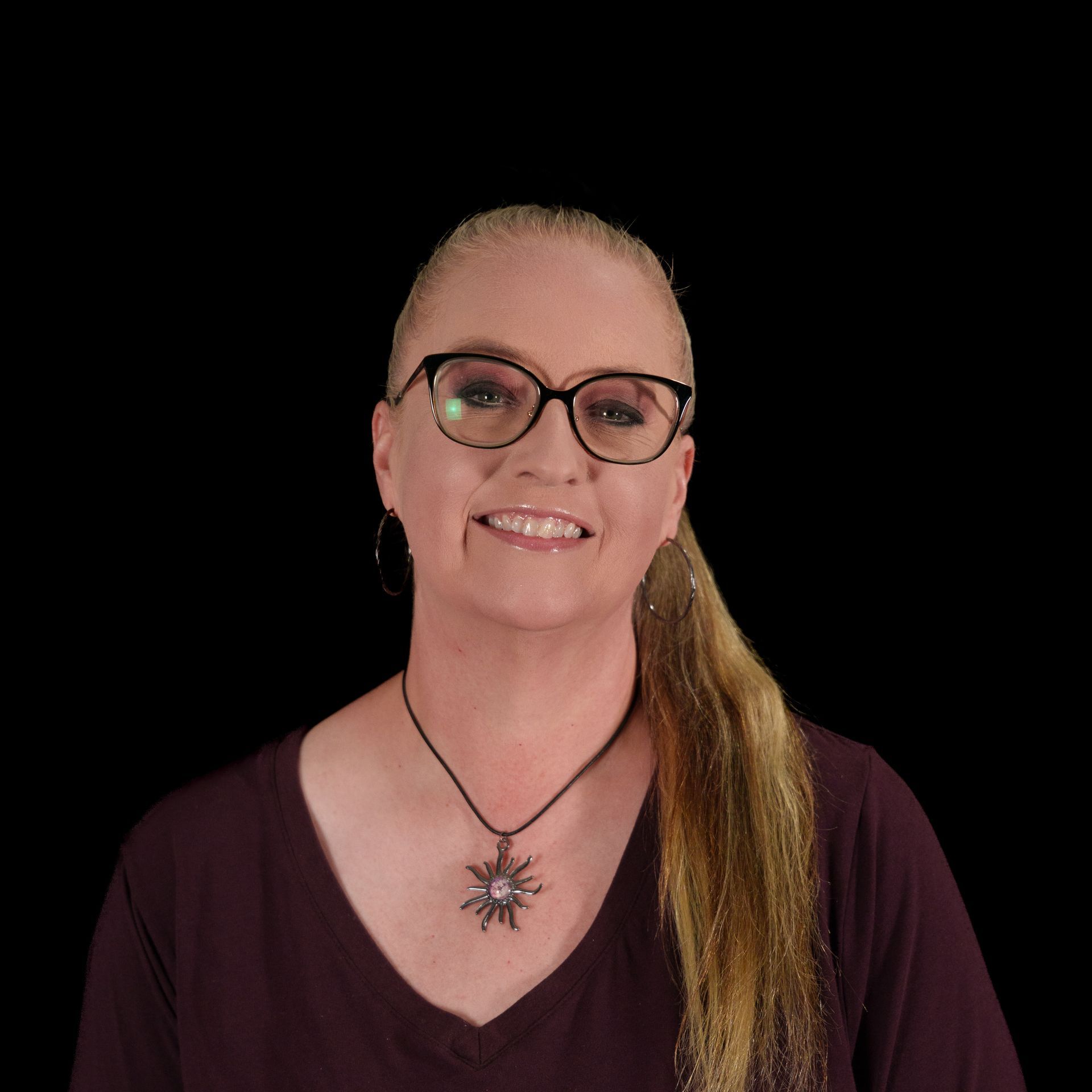 Woman wearing glasses, smiling, with a high ponytail and a black shirt that says 