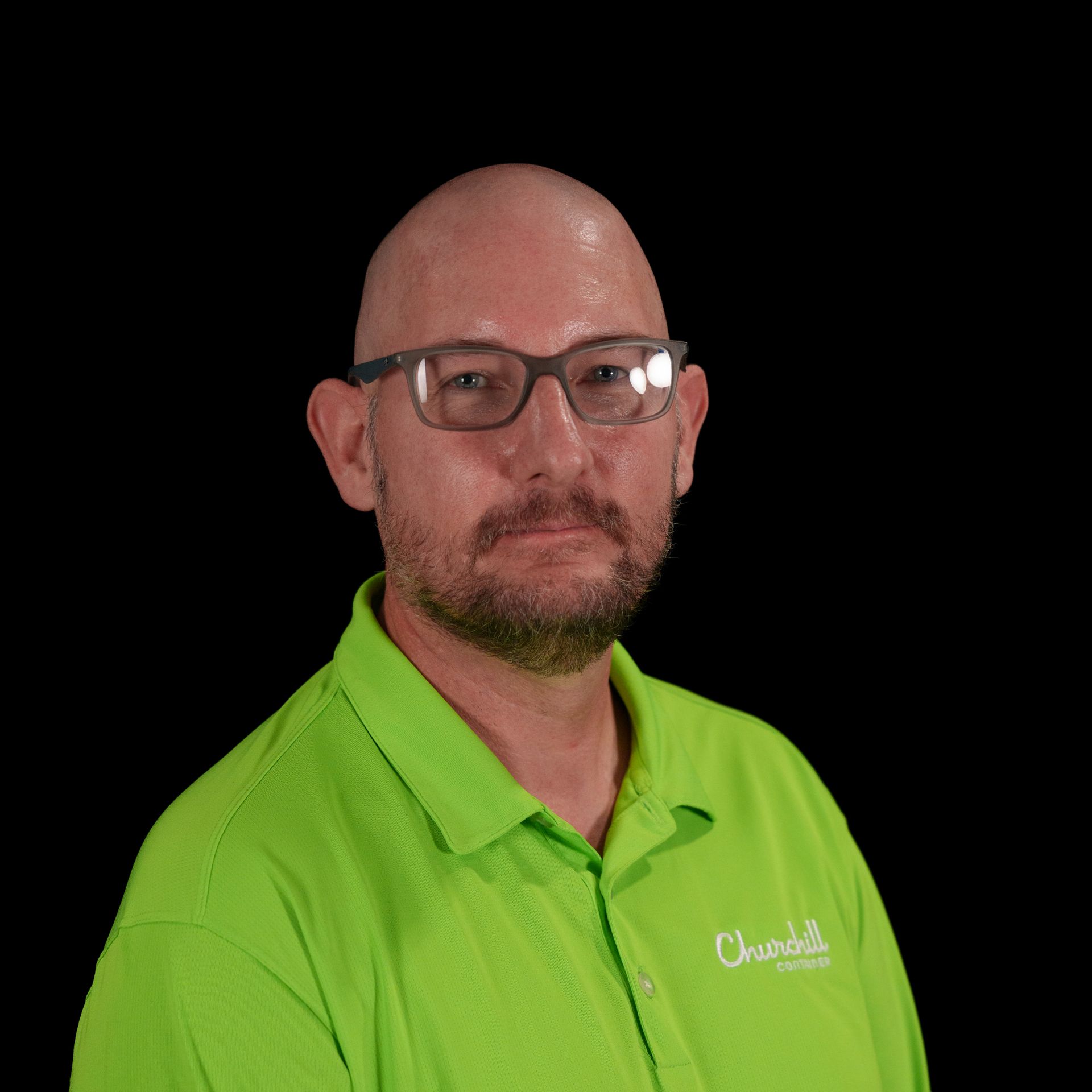 Man with a beard and glasses smiles, wearing a green shirt, against a black background.