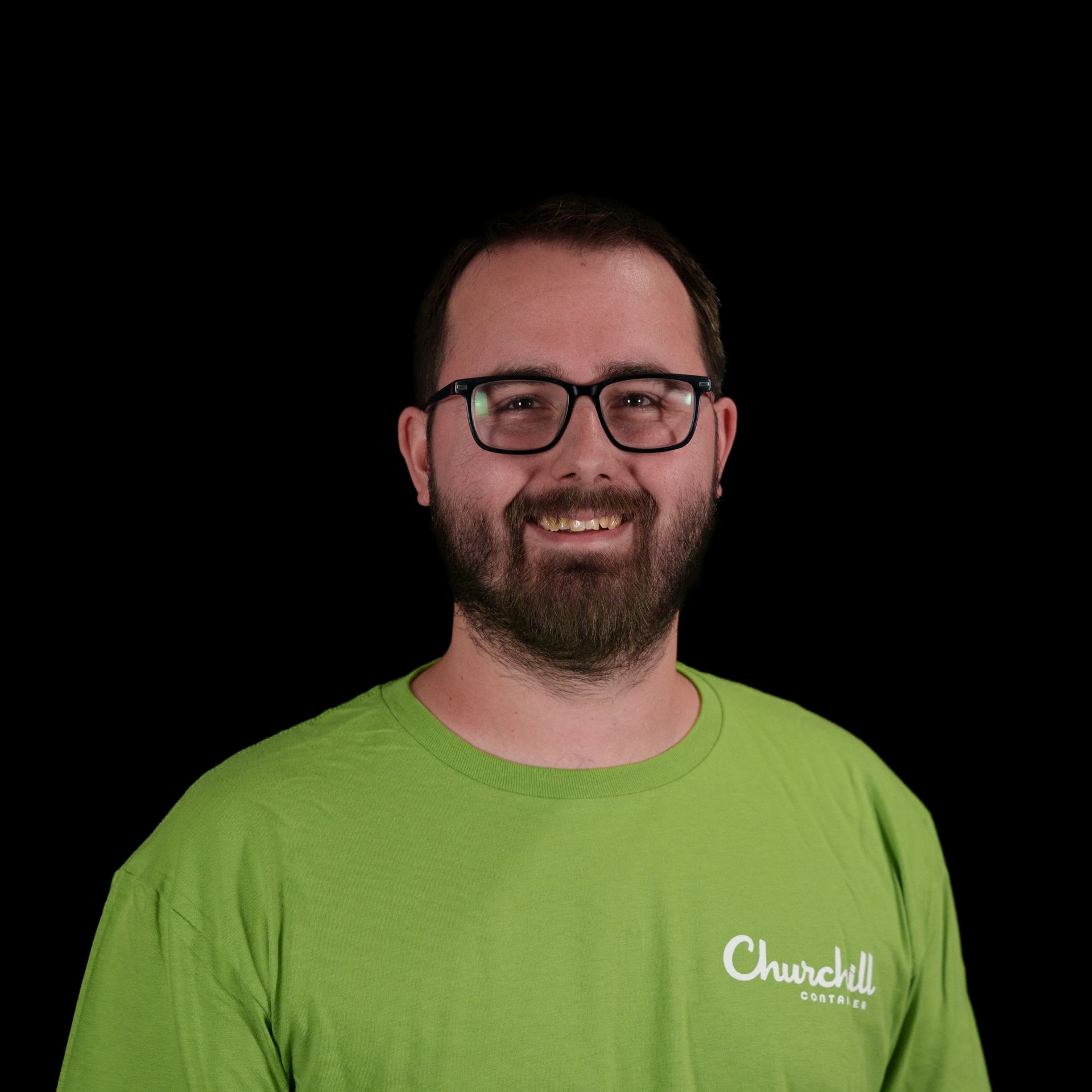Man with glasses and beard against a black background. He is wearing a dark t-shirt and smiling slightly.