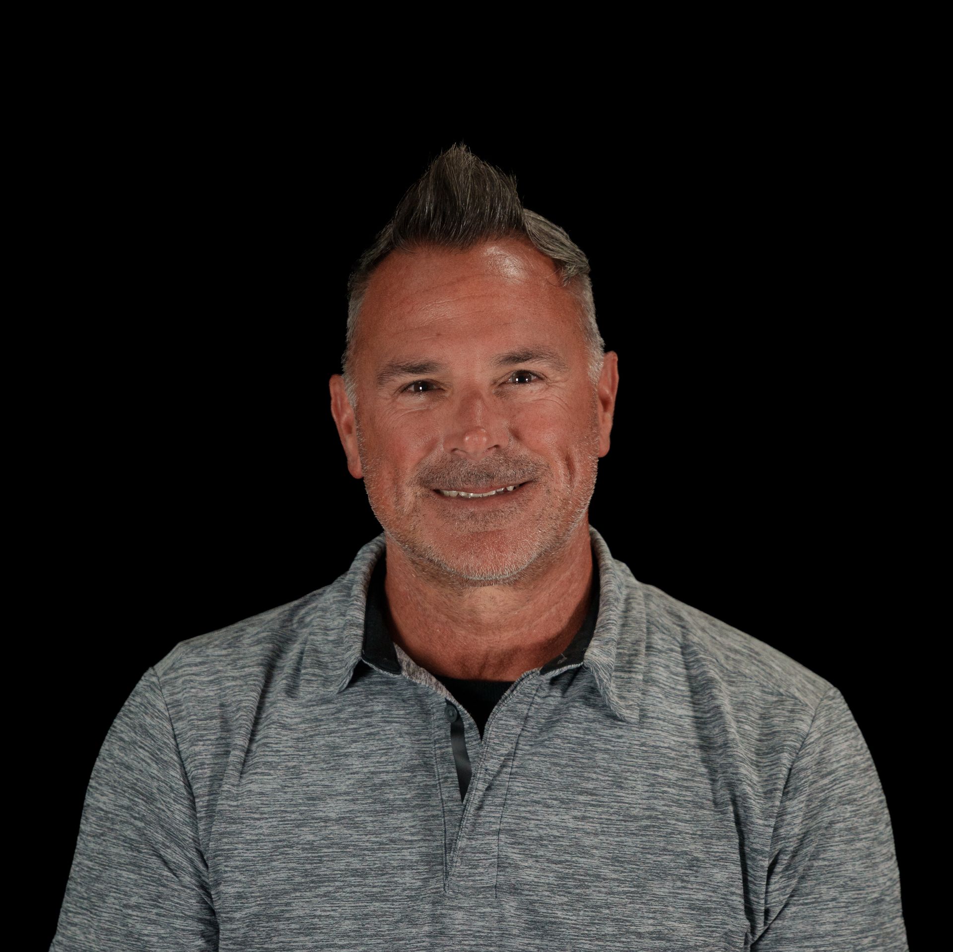 Man smiling, wearing a gray and black vest, against a black background.