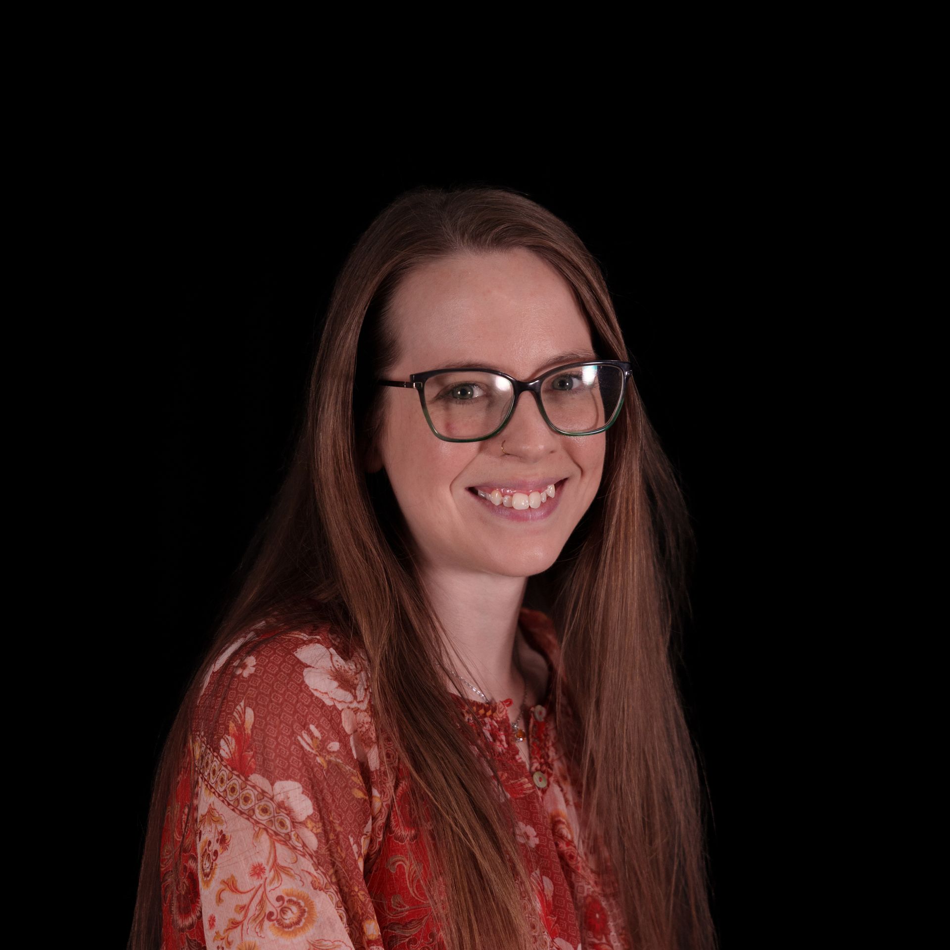Woman with glasses smiling, wearing a gray zip-up shirt against a black background.