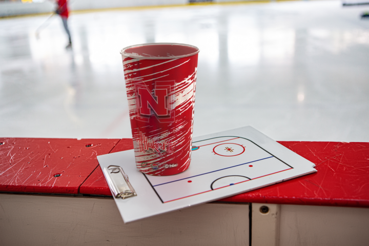 Hand holding a Chiefs cup at a stadium, with red seats and field in the background. Cup reads