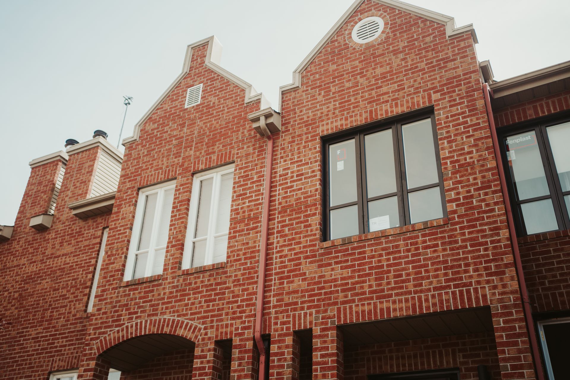 Façades de maisons de ville en briques rouges, fenêtres à encadrement blanc et pignons à redents sous un ciel pâle