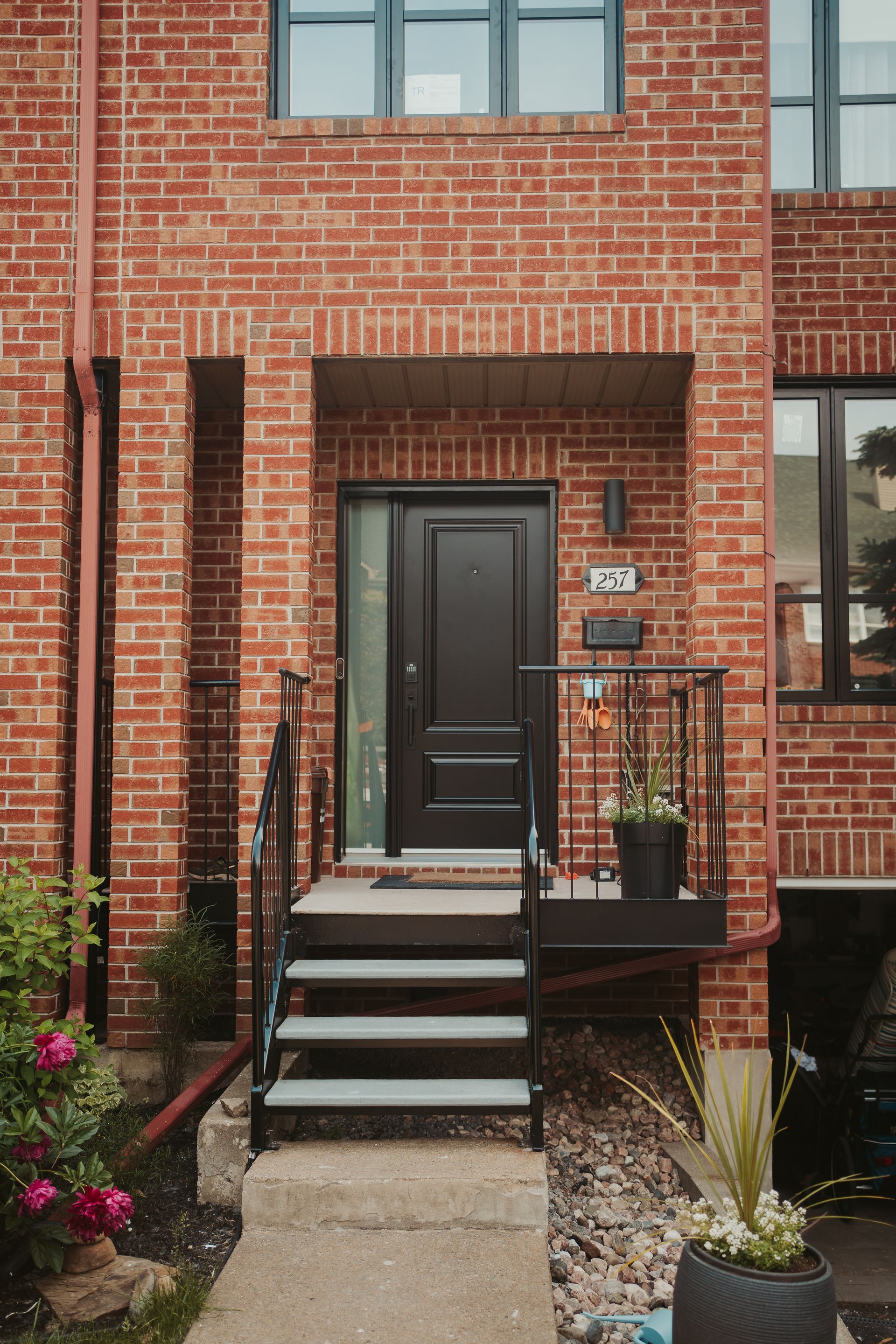 Brick townhouse entrance with black front door, small stoop, and steps leading from a walkway