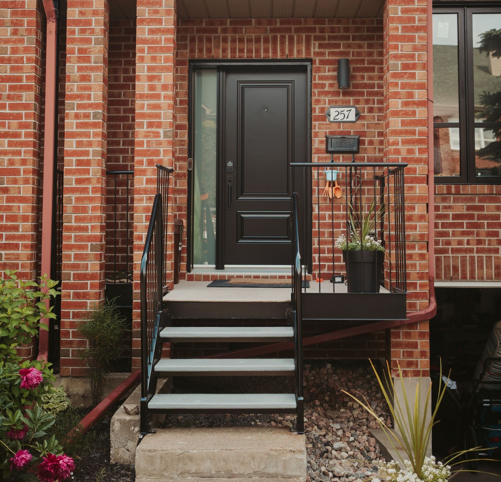 Entrée d'une maison de ville en briques avec porte noire, marches d'entrée, balustrade et plante en pot