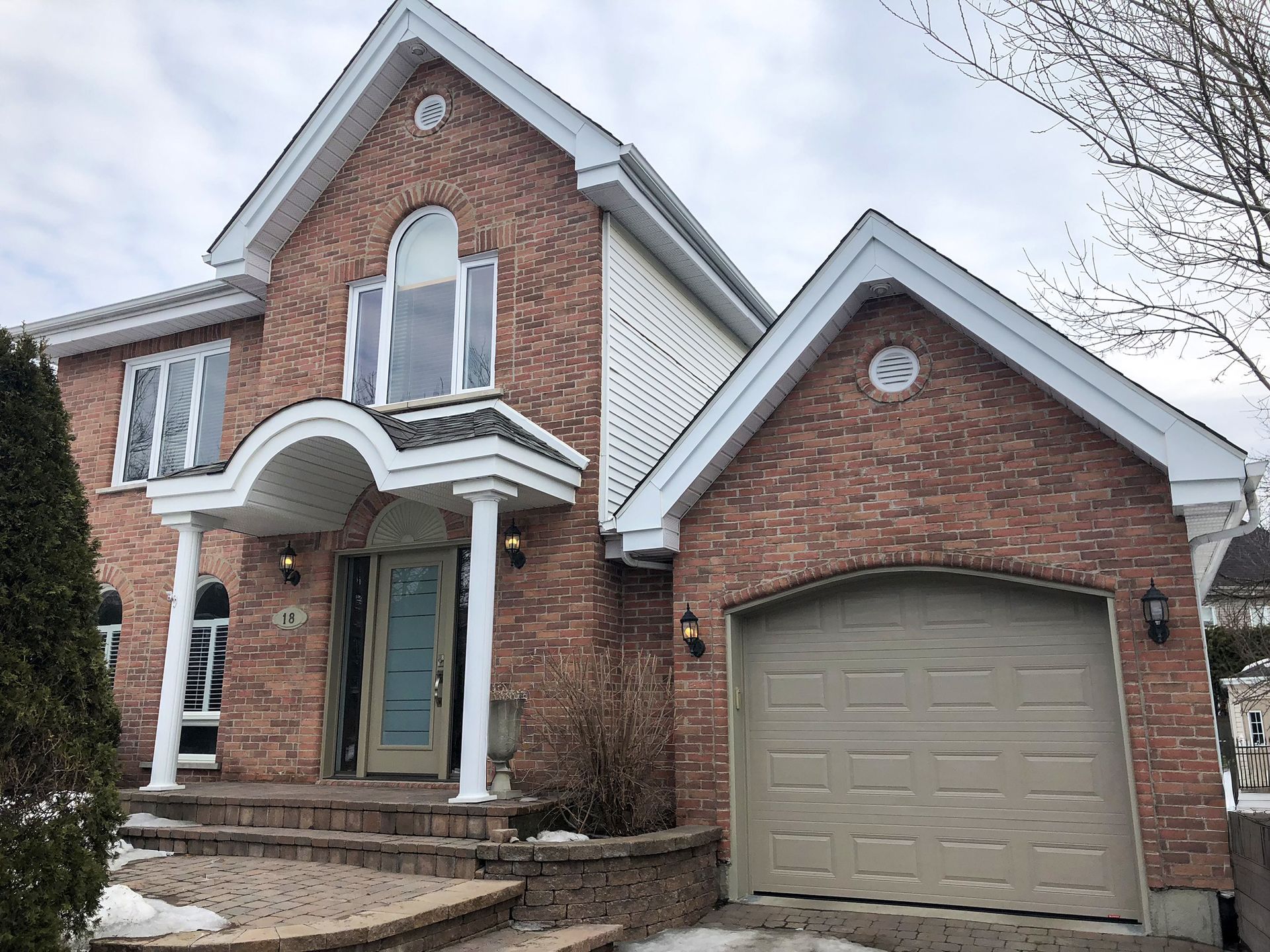 Brick two-story house with arched front entry, green door, and attached garage in winter.
