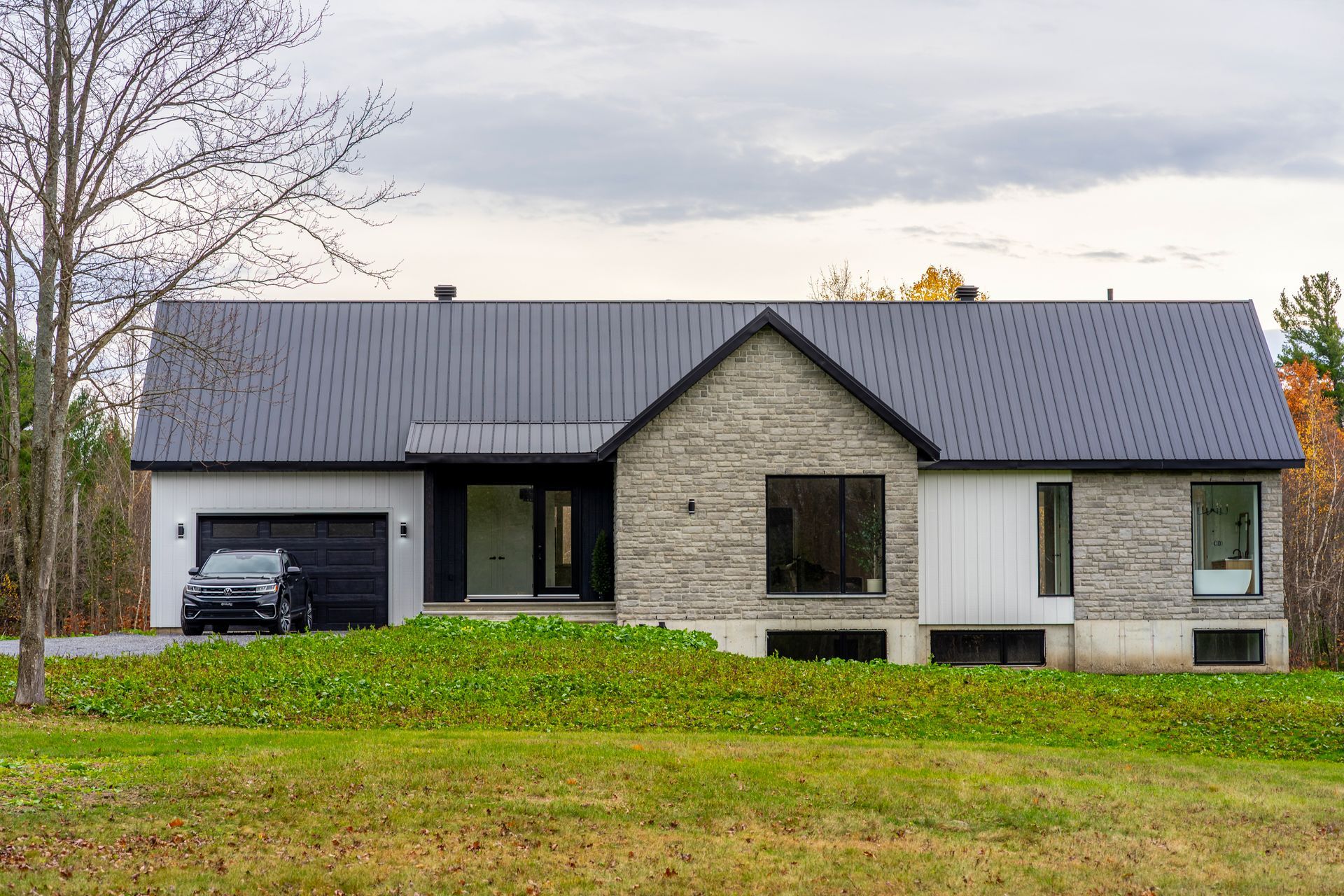 Maison moderne de plain-pied avec toit gris, garage noir et cour avant gazonnée sous un ciel nuageux