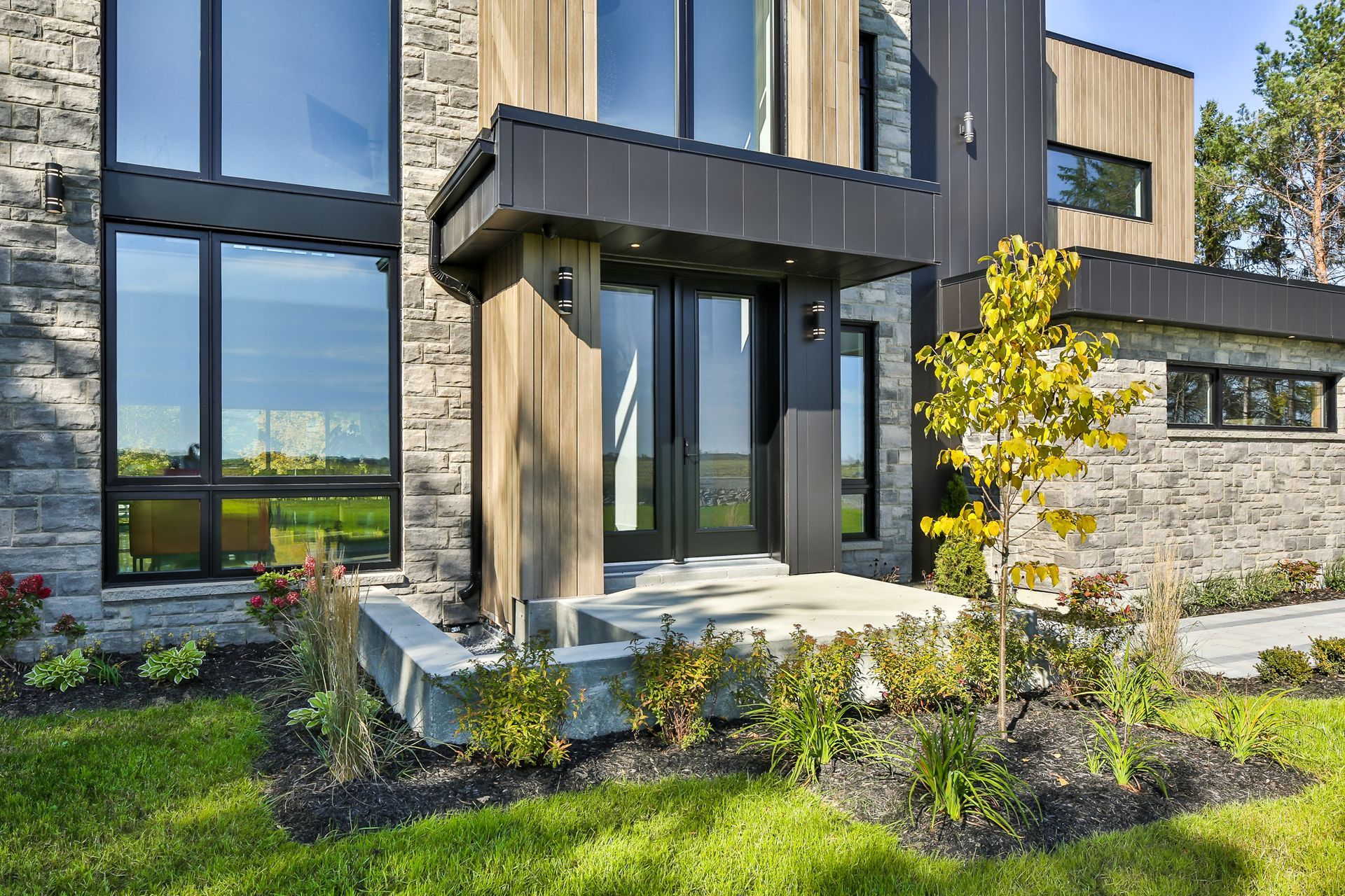 Extérieur d'une maison moderne à deux étages avec fenêtres à cadre noir, bardage en bois et jardin paysager à l'avant.