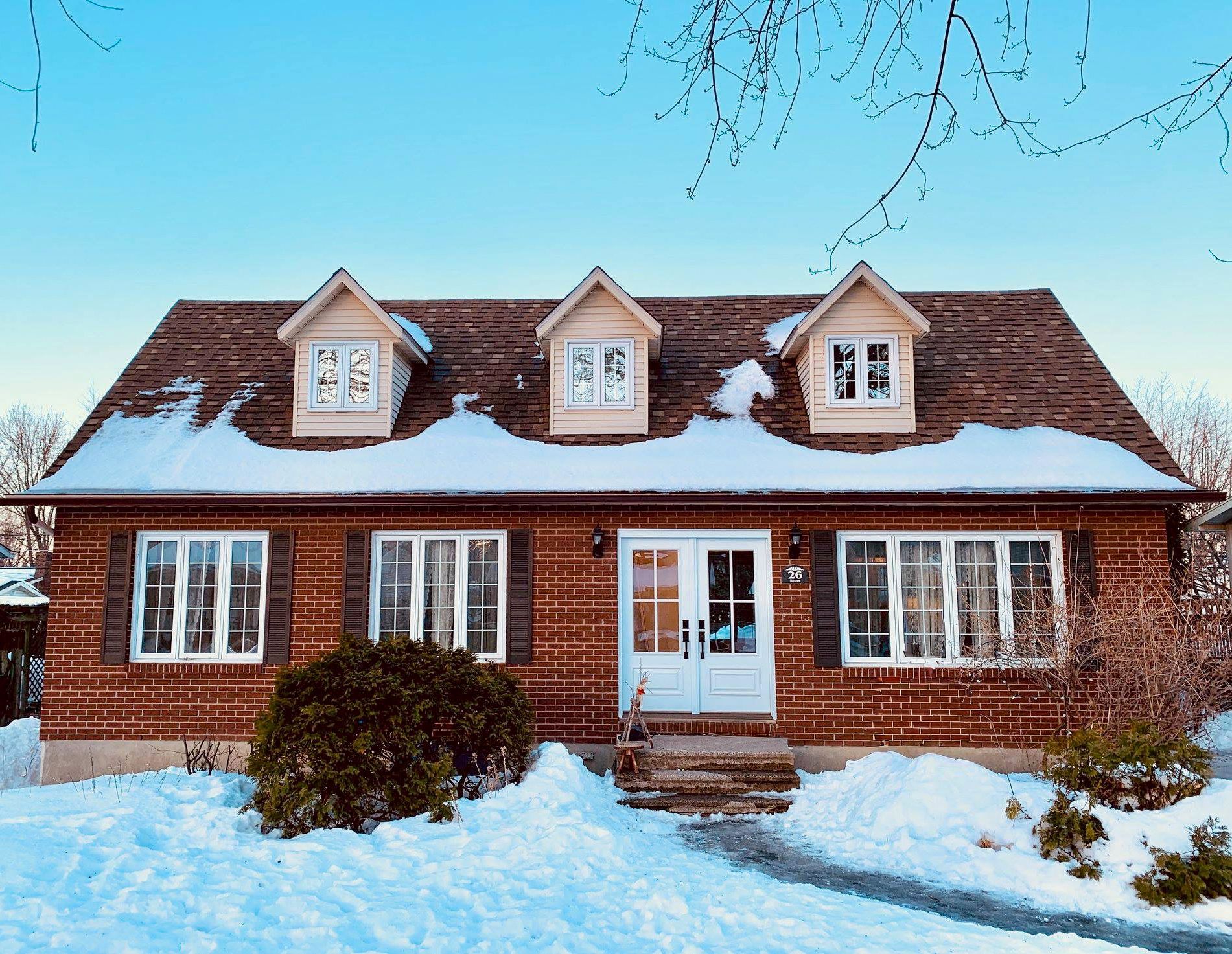 Maison en briques enneigée avec un porche blanc et des lucarnes sous un ciel d'hiver dégagé