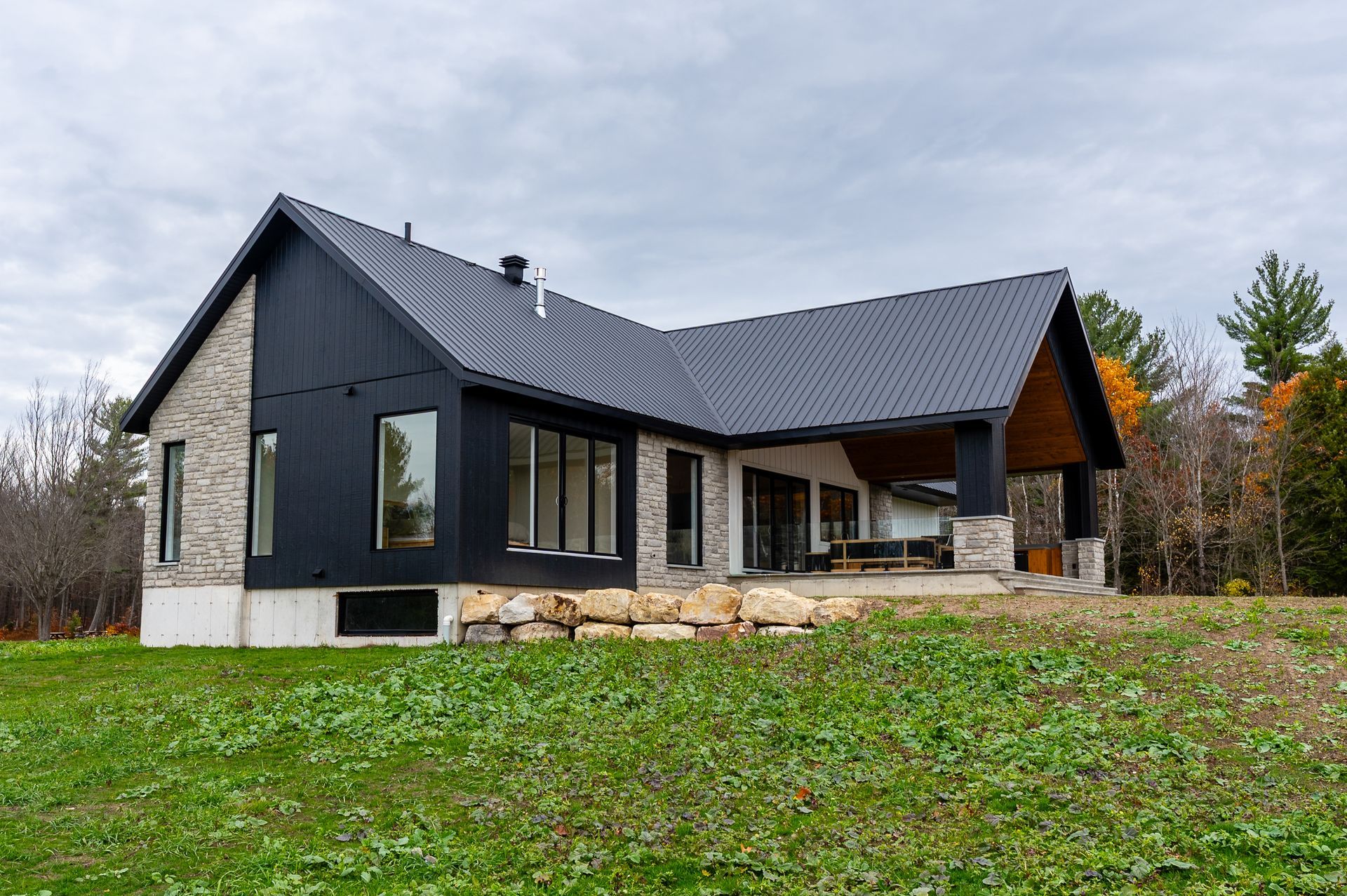 Modern black house with stone accents on a grassy lot under an overcast sky