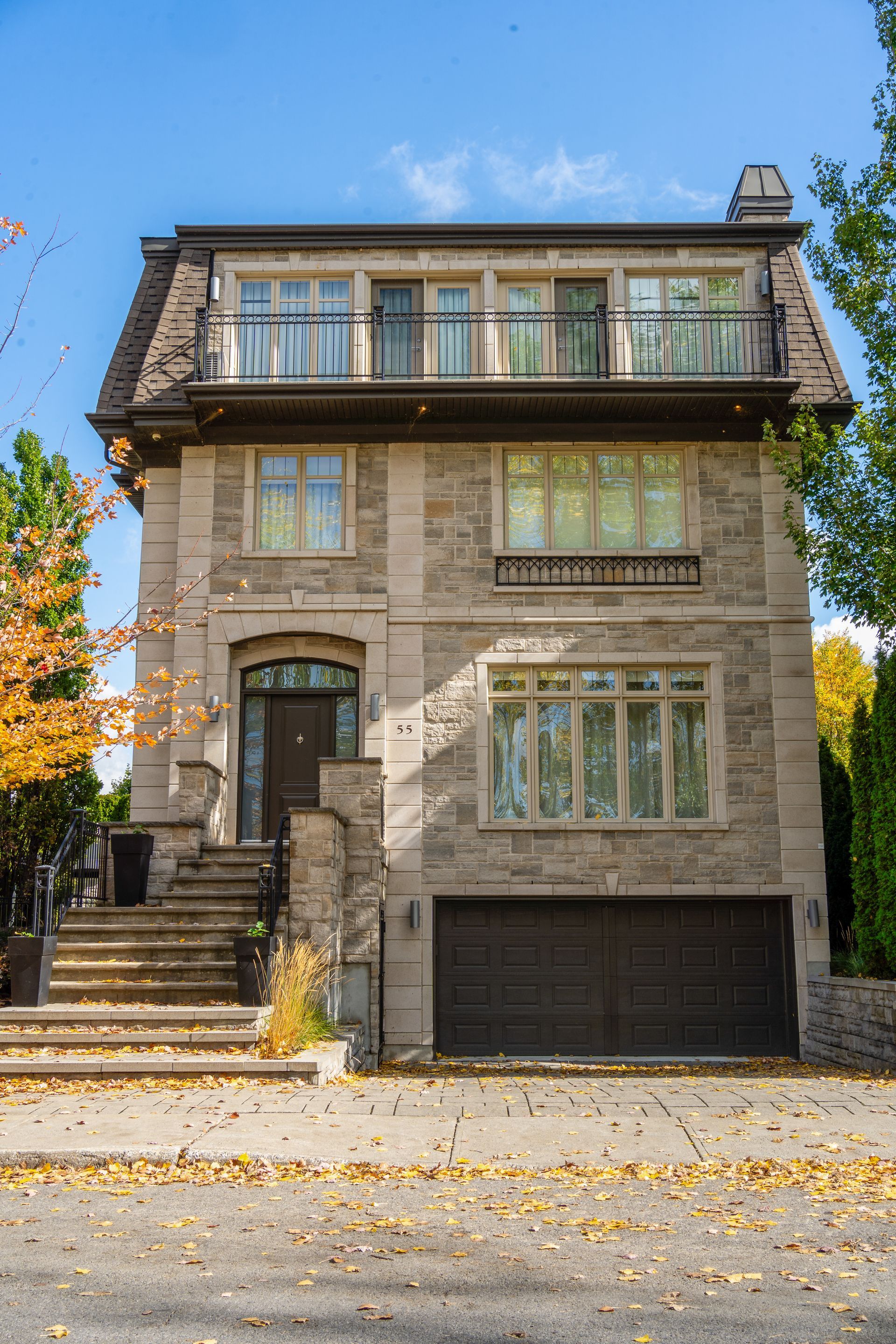 Stone house with large windows, front stairs, and a garage under a blue sky with autumn leaves.