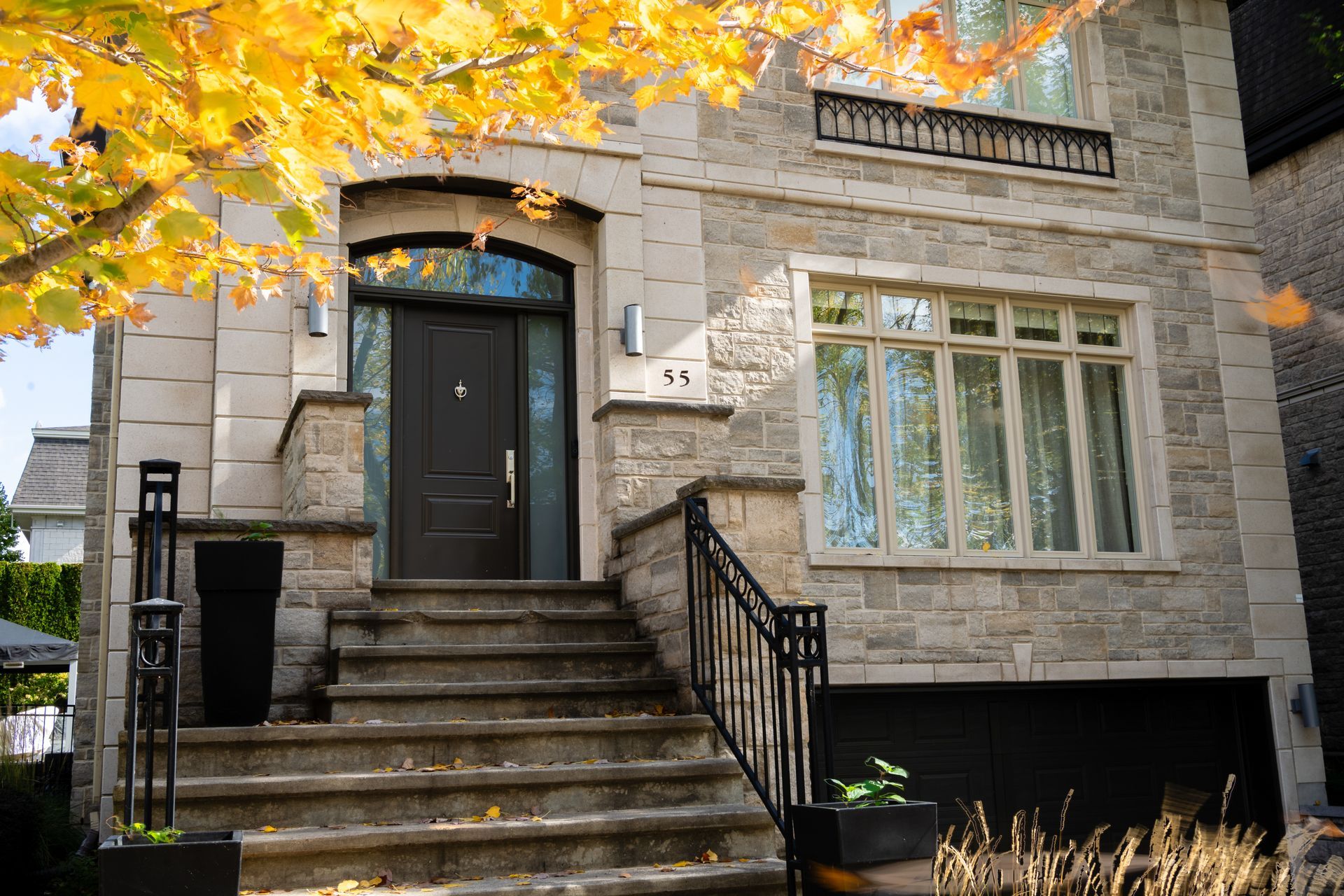 Entrée d'une maison en pierre avec porte noire, marches d'entrée et feuilles d'automne au-dessus