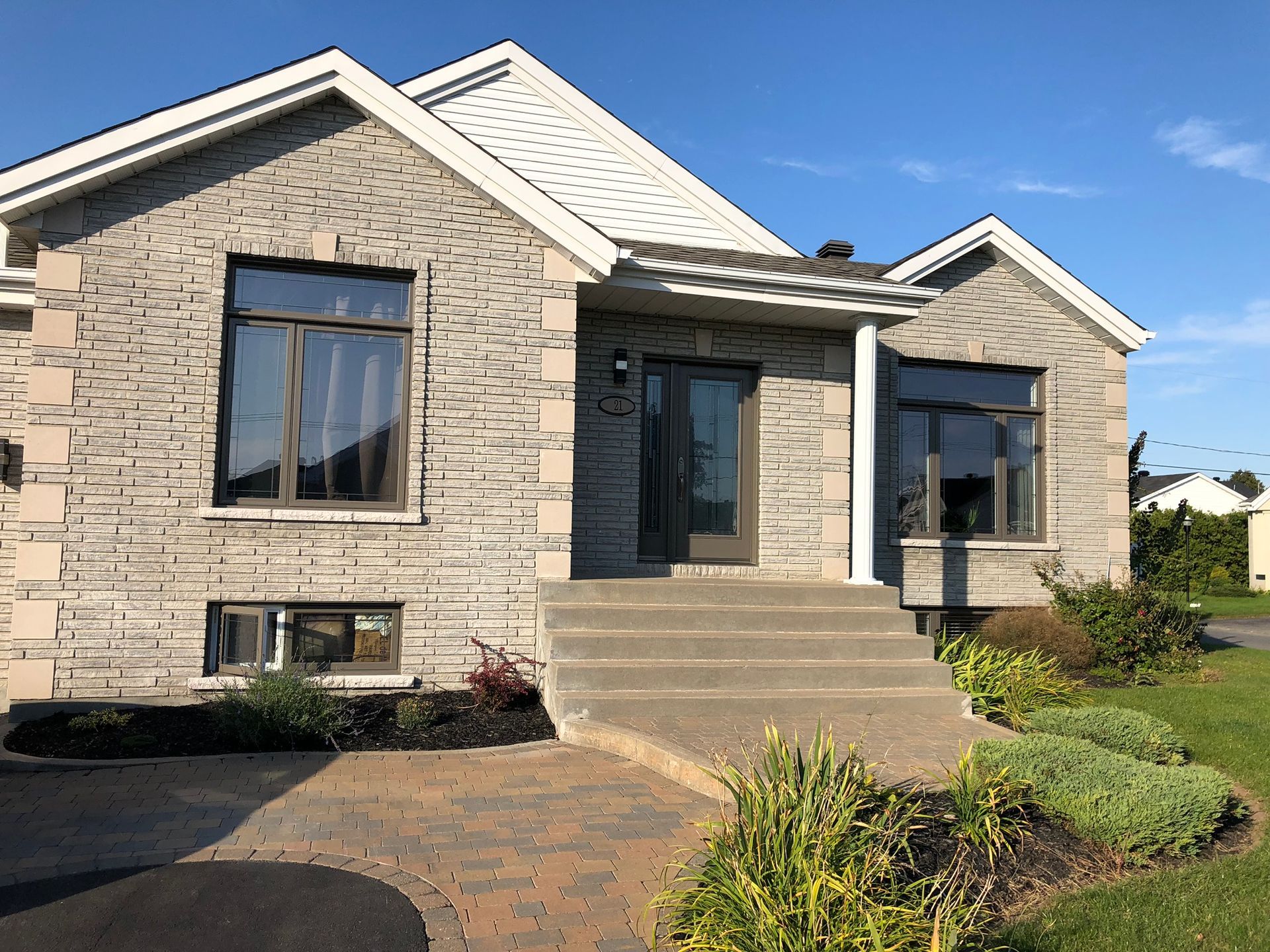 Stone house exterior with front steps, large windows, and a paved driveway in bright sunlight