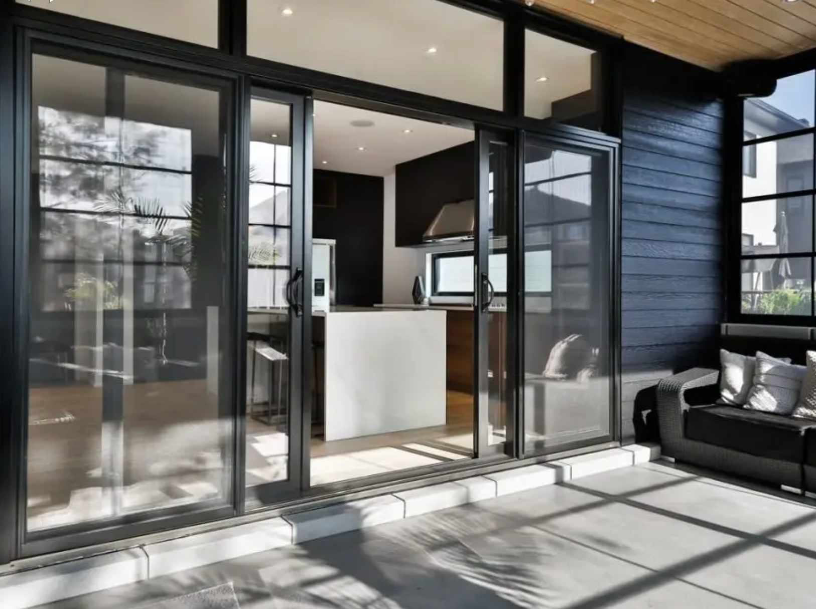 Modern glass patio doors open to a bright, minimalist kitchen with sunlit outdoor seating