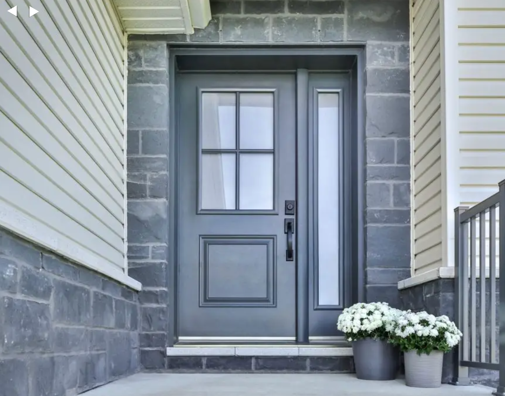 Gray front door with sidelights, white trim, and potted white flowers on a porch