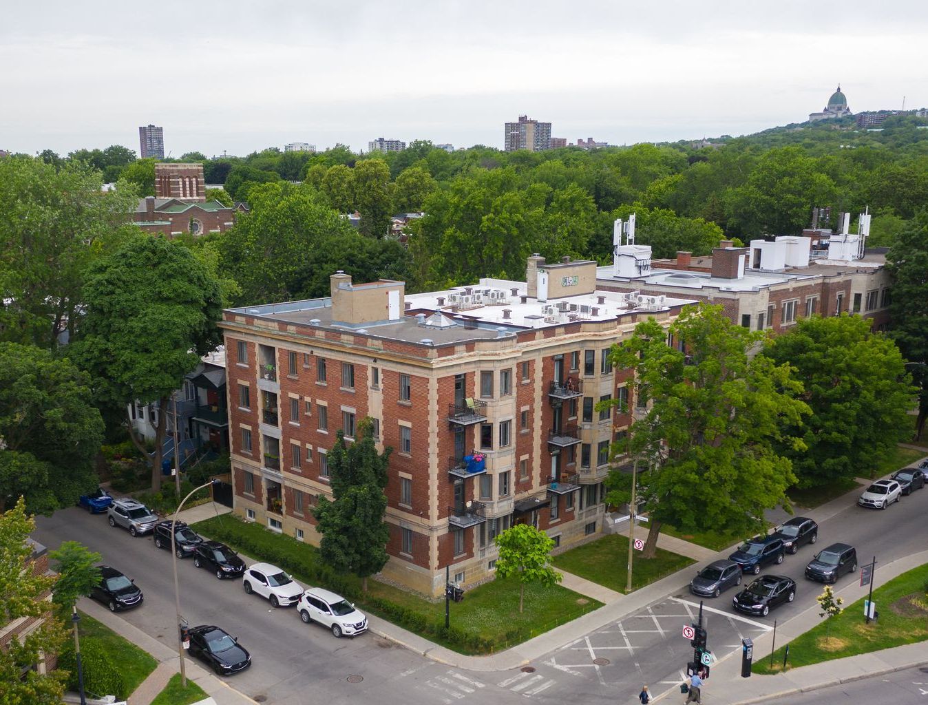 Aerial view of a brick apartment building surrounded by trees at a city street corner