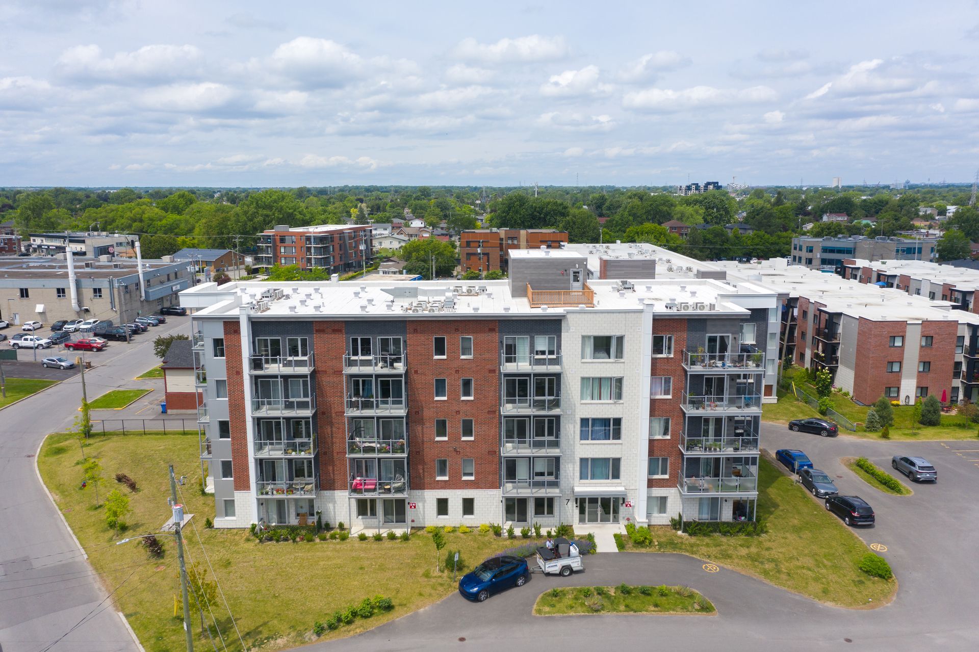 Aerial view of a red-brick apartment building with balconies and parked cars on a cloudy day