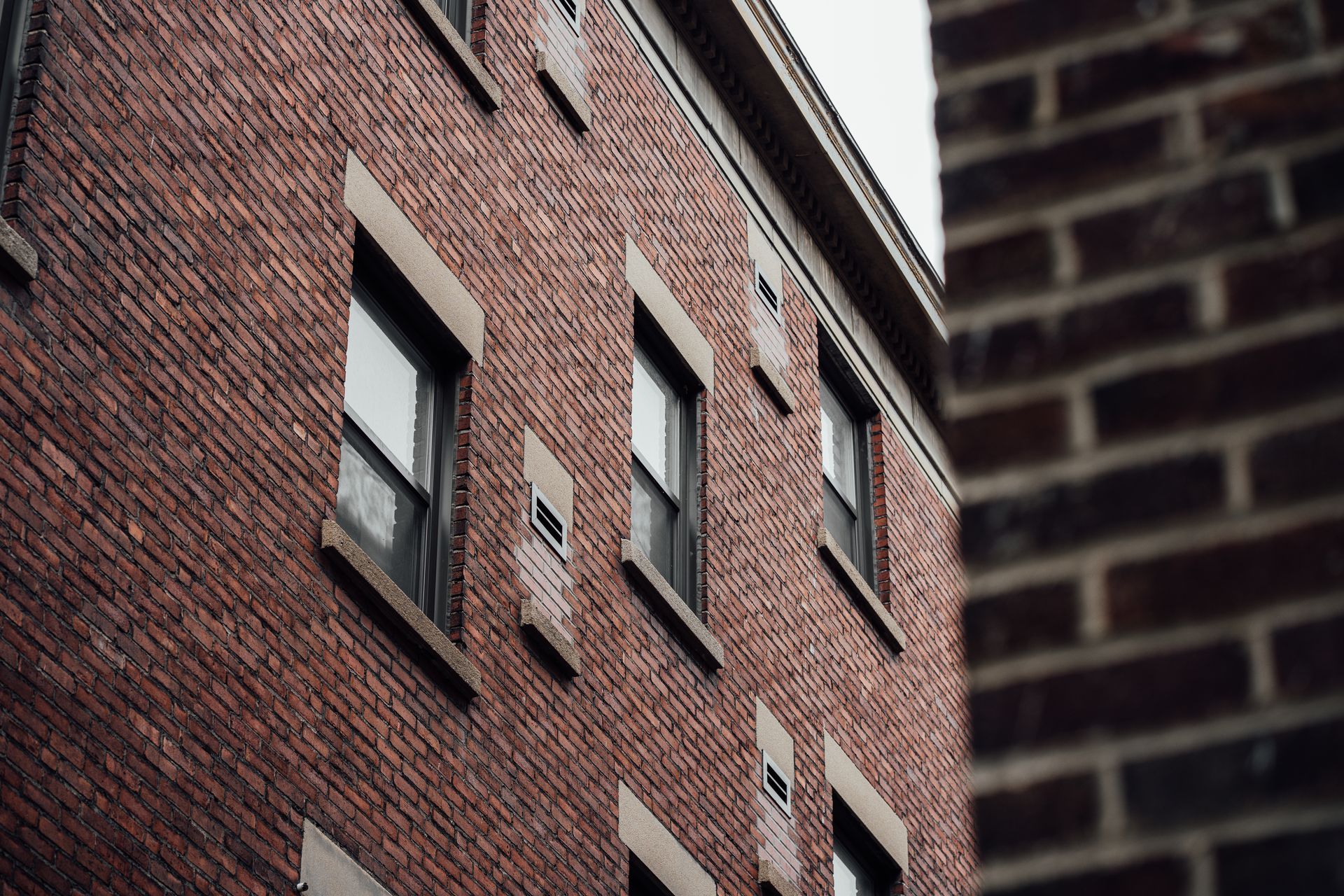 Red brick apartment building seen from an alley, with windows and a dark brick wall in the foreground.