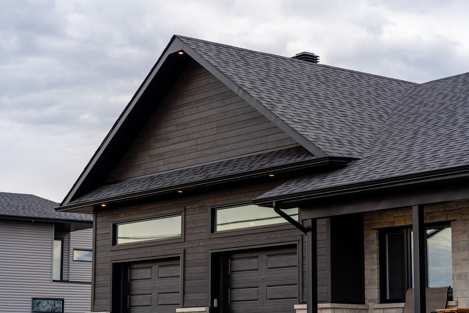 Dark gray shingled house roof with triangular gable and dormer windows under cloudy sky