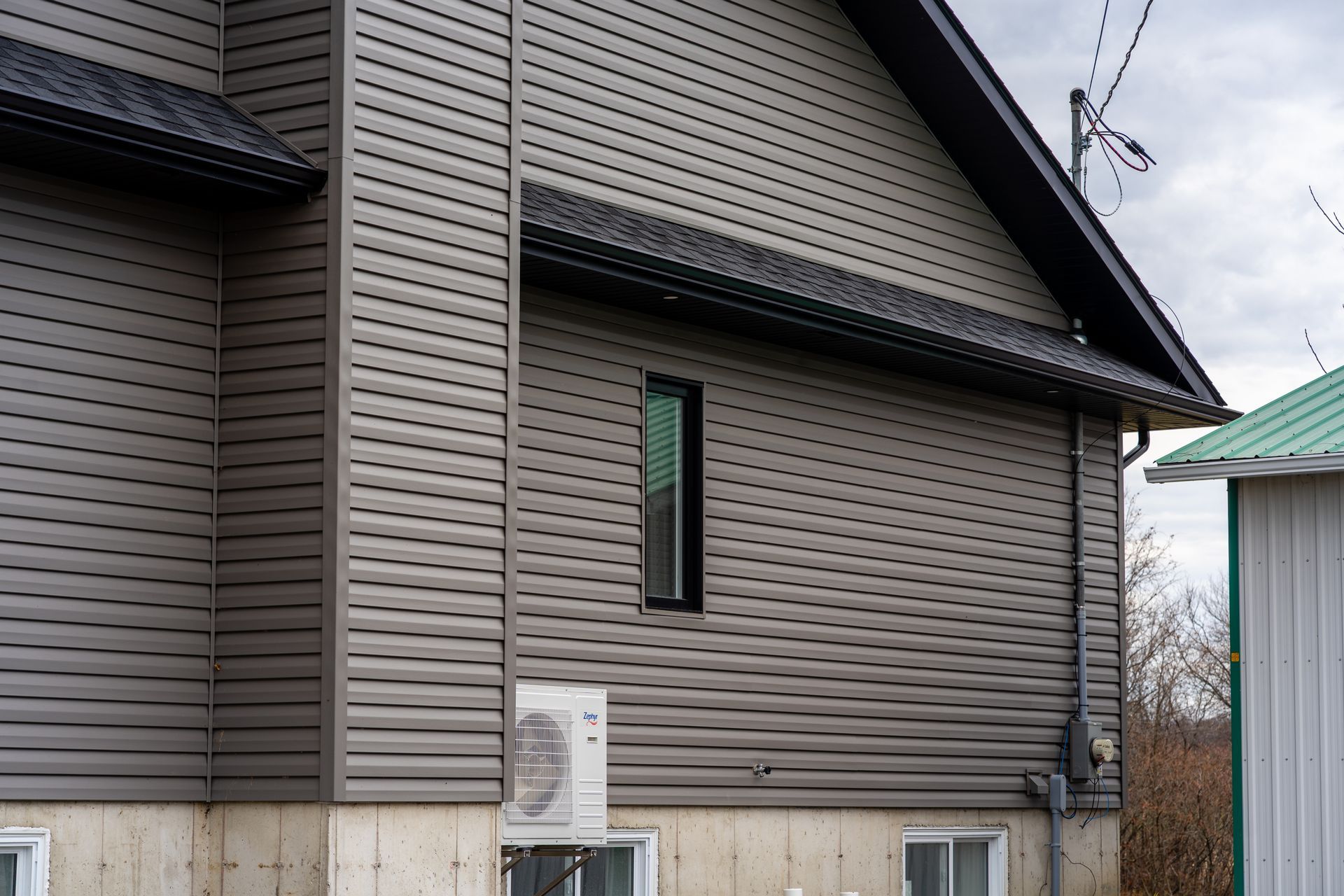 Côté d'une maison grise avec bardage, une fenêtre étroite et un climatiseur extérieur près du mur.