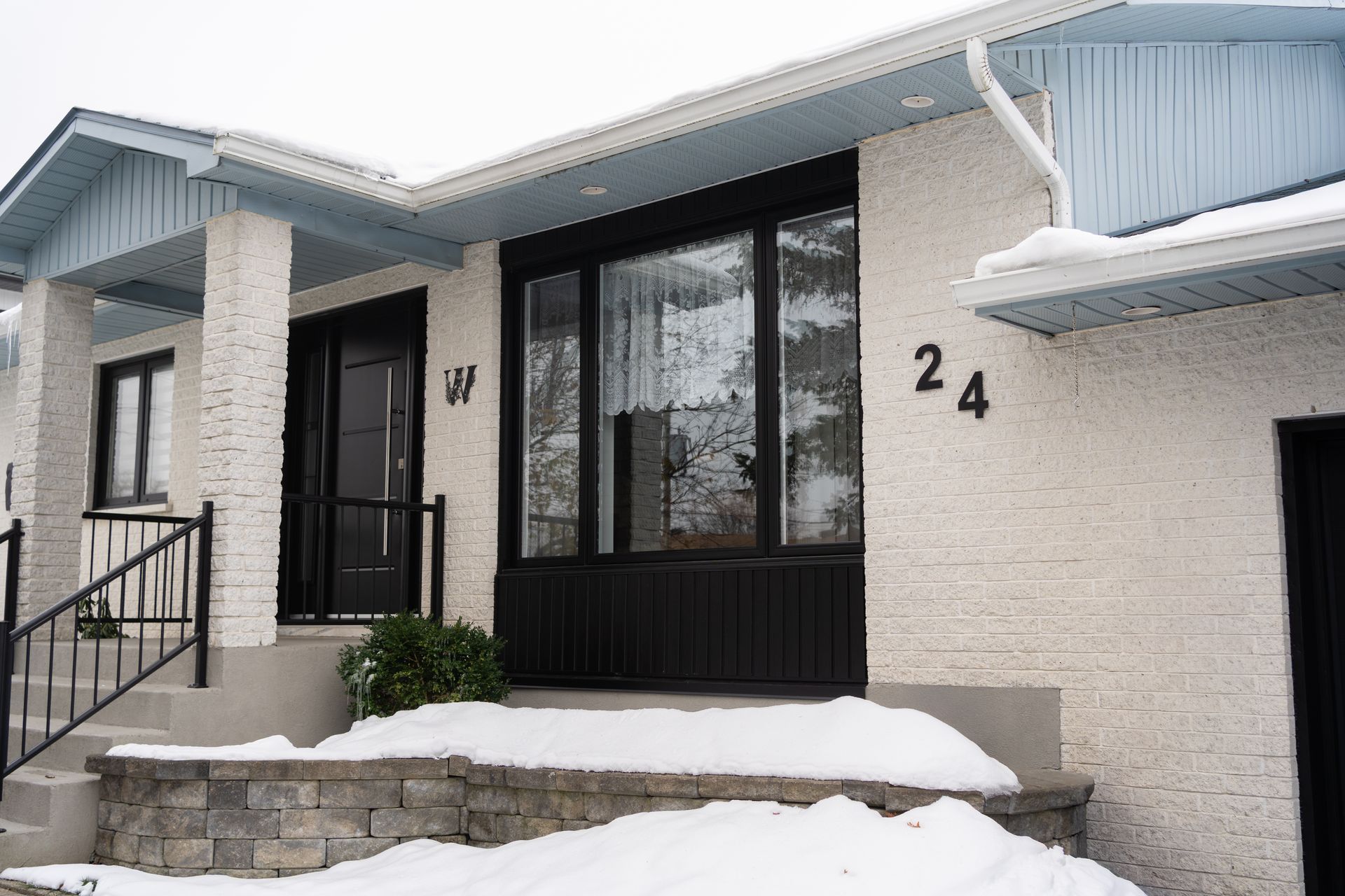 Snow-covered house entrance with black-framed windows and the number 24 on the wall