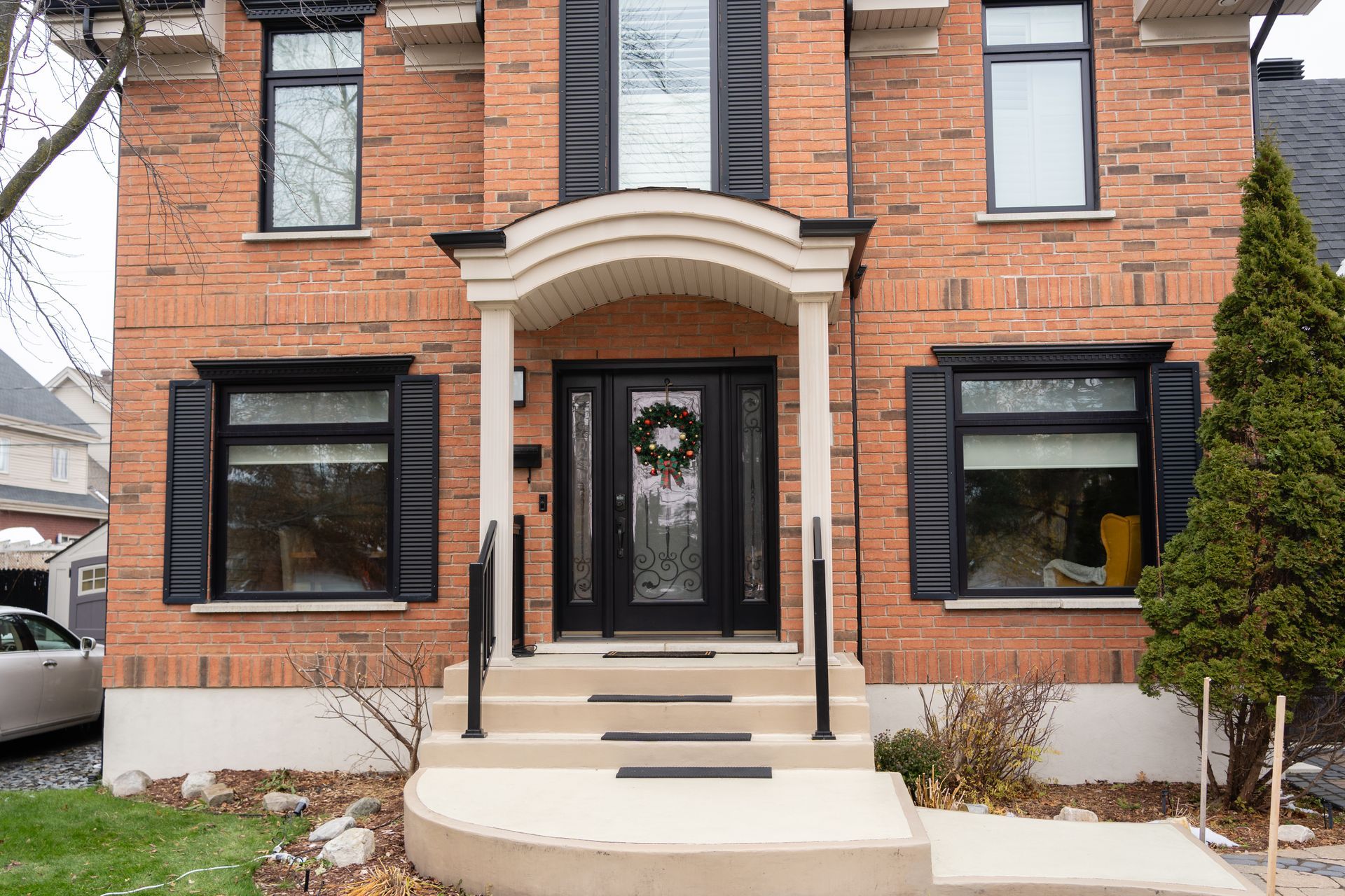 Red brick house entrance with black shutters, curved awning, and front steps with railings