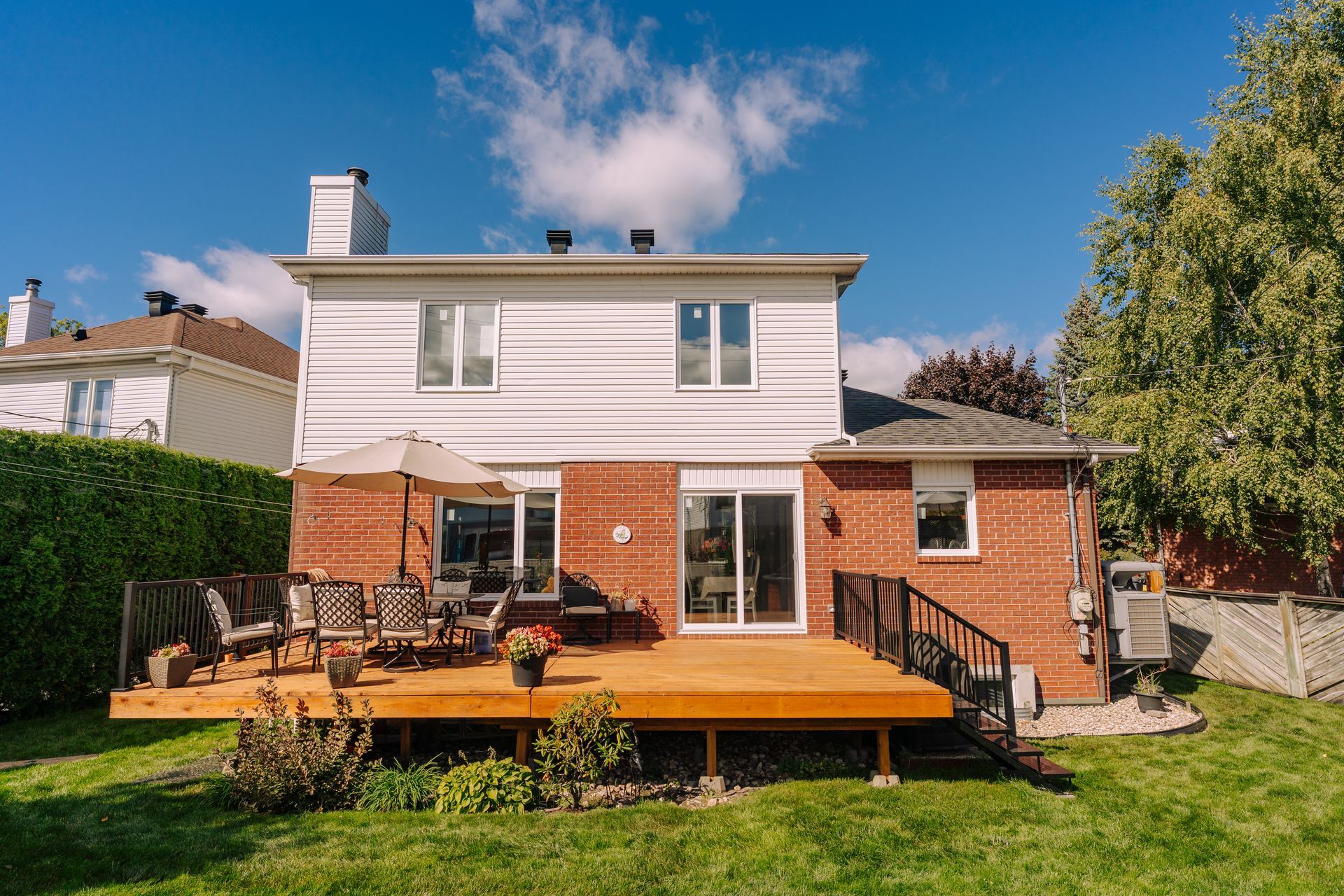 Terrasse et patio à l'arrière d'une maison blanche en briques de deux étages, avec mobilier de jardin et pelouse verdoyante.