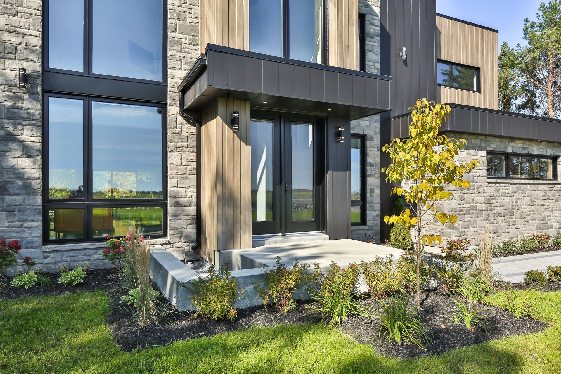 Extérieur de maison moderne avec de grandes fenêtres, des éléments en pierre et un jardin paysager à l'avant.
