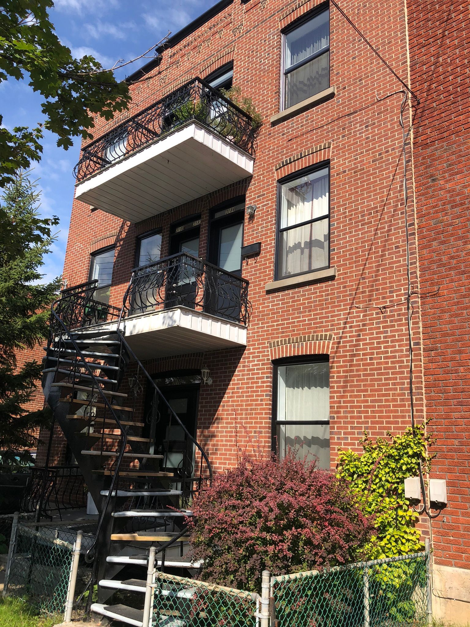 Brick apartment building with black fire escape and white balconies, viewed from below on a sunny day