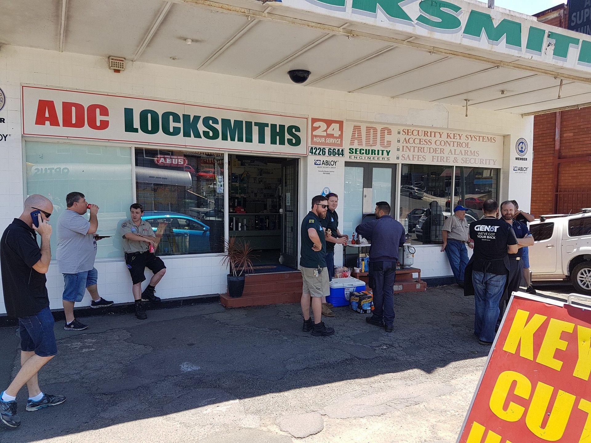 A group of men are standing in front of a shop — ADC Locksmiths in Wollongong, NSW 
