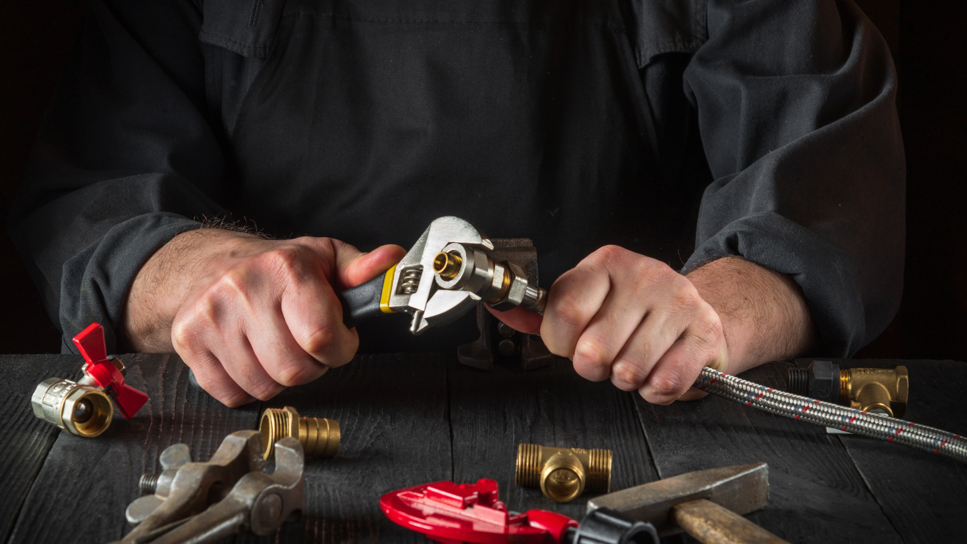 A man is sitting at a table working on a pipe with a wrench.