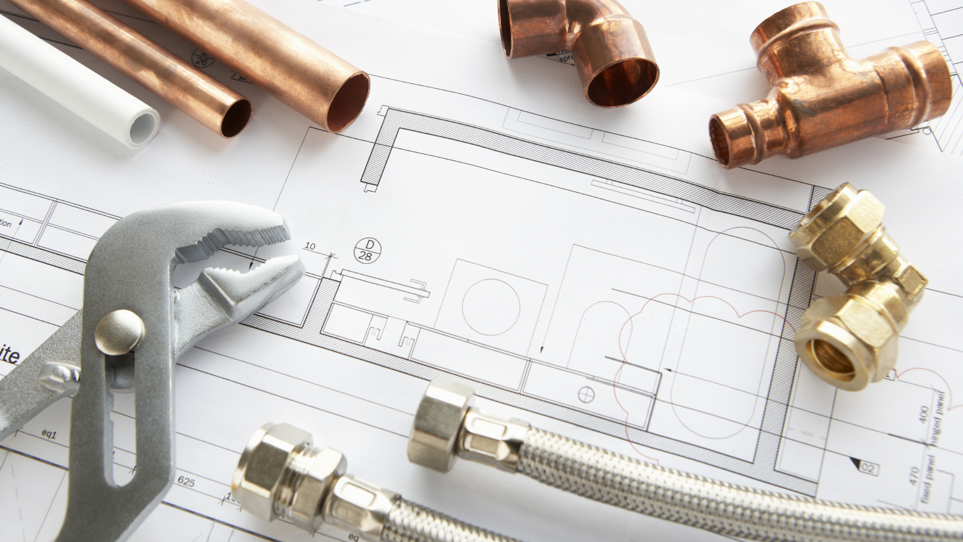 Copper pipes and fittings are laying on top of a blueprint.