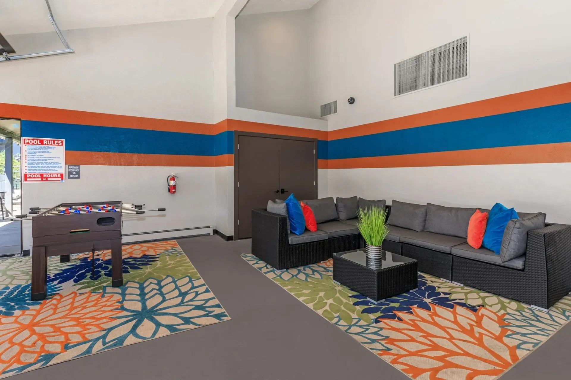 Modern lobby with gray sofas, colorful pillows, side table, and foosball table on patterned carpet.