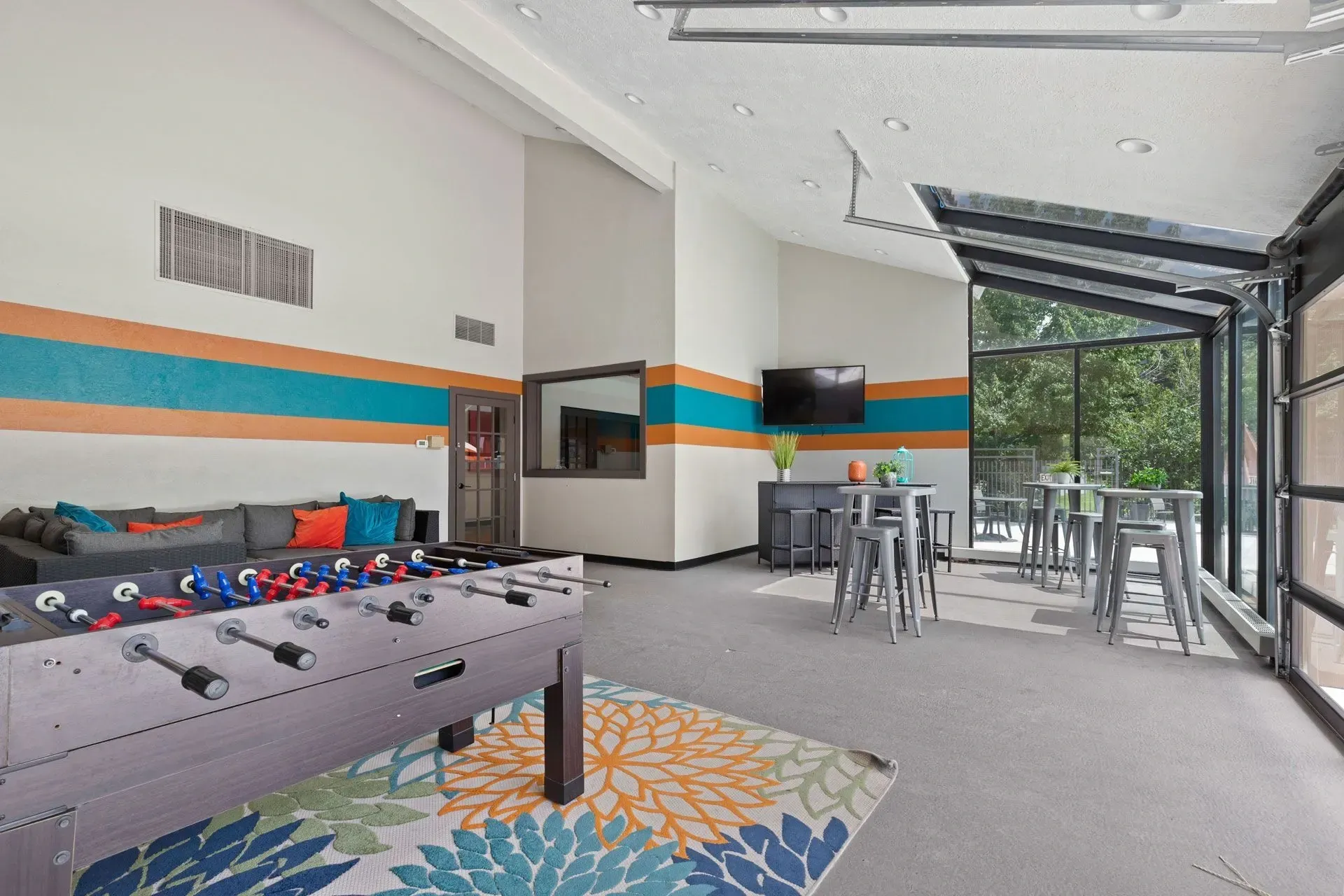 Recreation room with foosball table, seating area, wall TV, and large open windows to a patio.