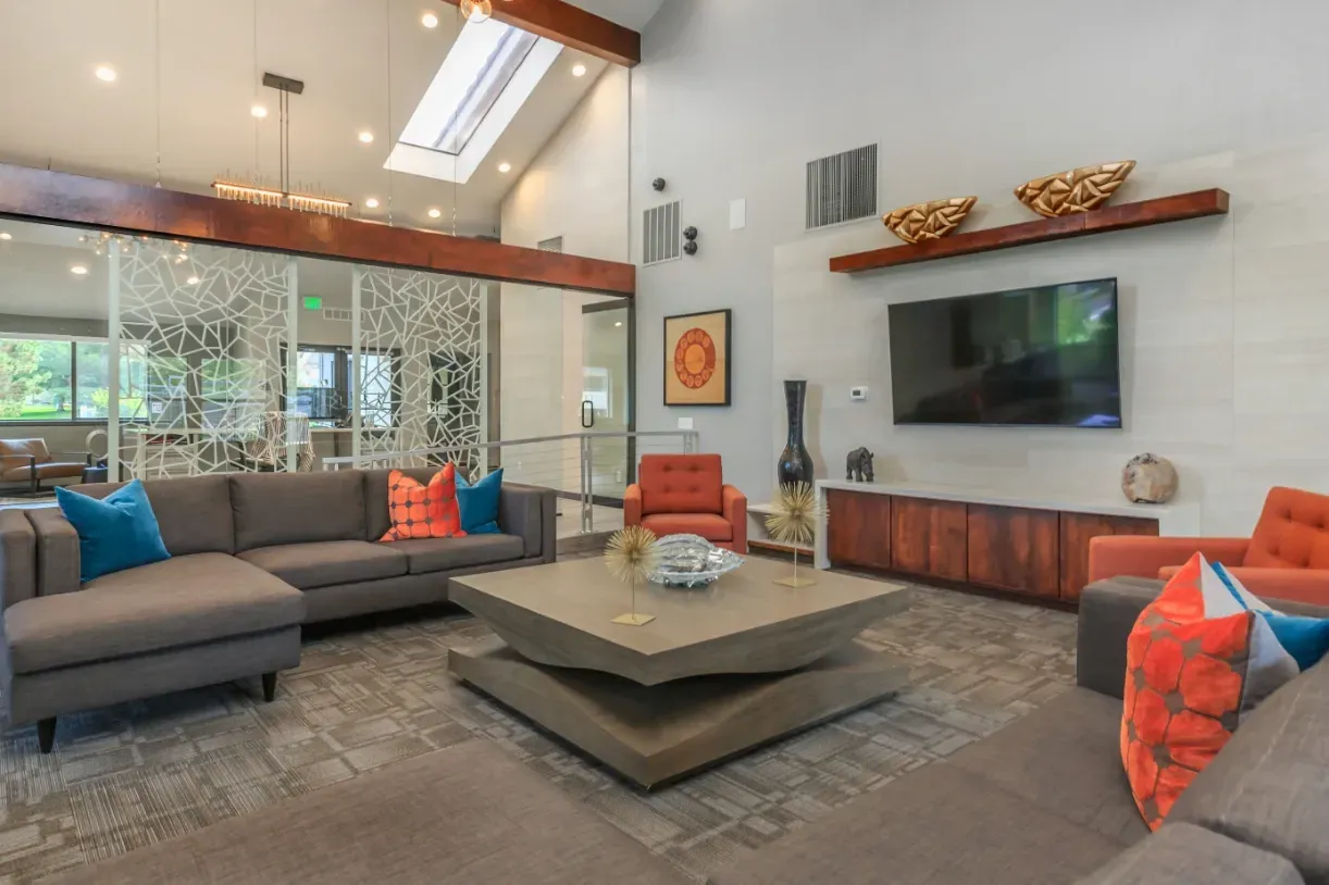 Modern communal lounge area with sectional sofa, armchairs, coffee table, and mounted TV.