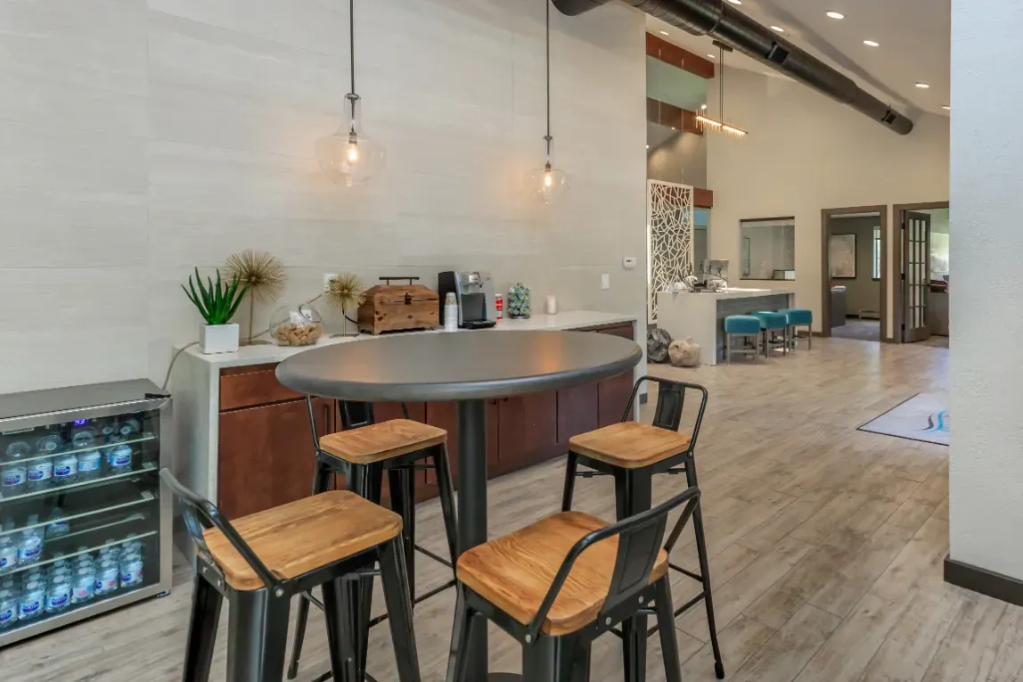 Community coffee bar with a table and chairs, a beverage cooler, and a counter with coffee amenities.