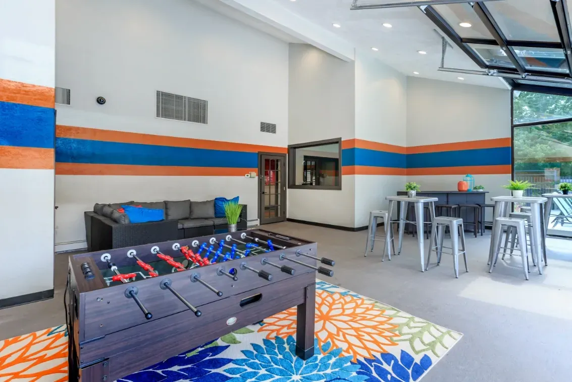 Community lounge area with a foosball table, sectional sofa, and high-top tables.