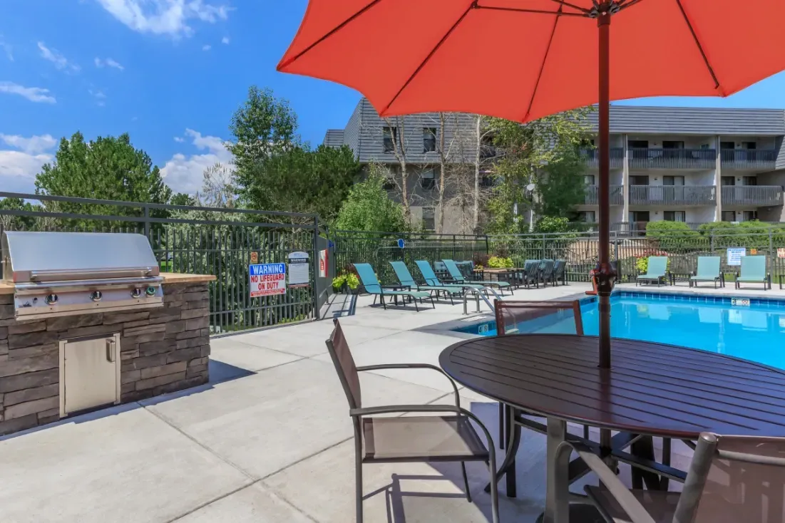 Outdoor swimming pool with lounge chairs, tables, and built-in grill.