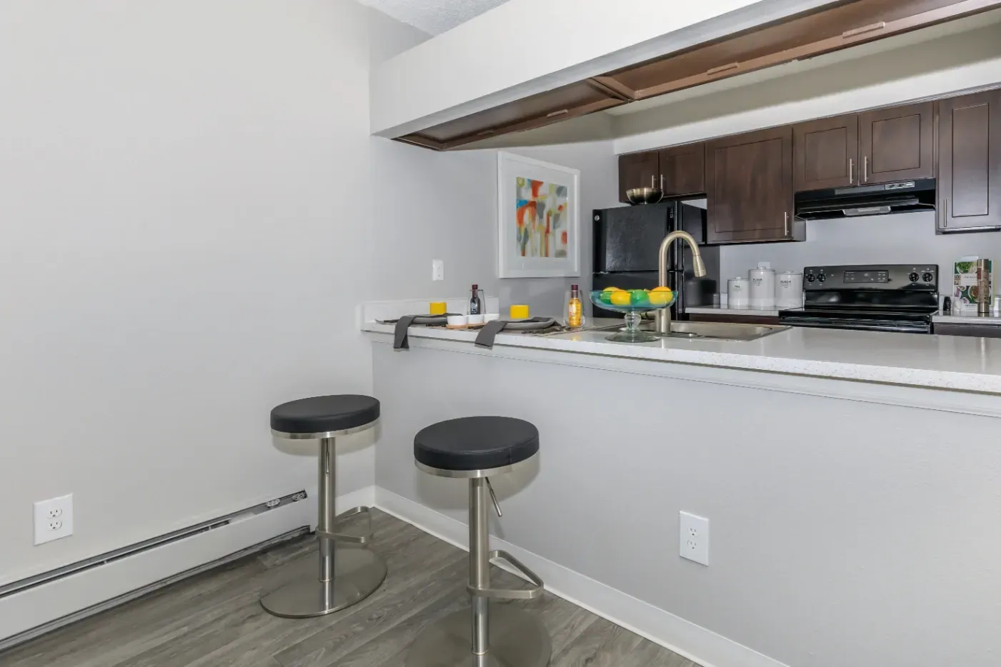 Modern kitchen with dark wood cabinets, black appliances, and a breakfast bar with two stools.