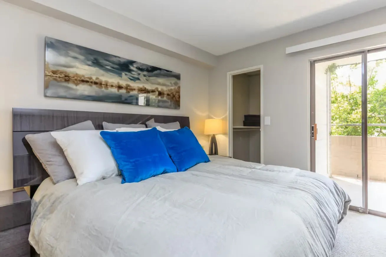 King size bed with blue and white pillows, modern headboard, closet, and sliding glass door leading to balcony.