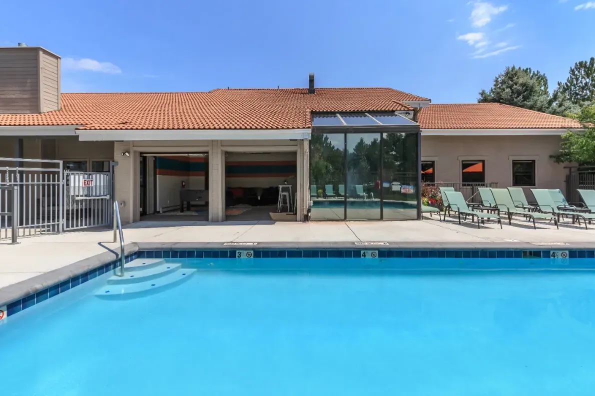 Outdoor swimming pool with lounge chairs and a covered area with tables.