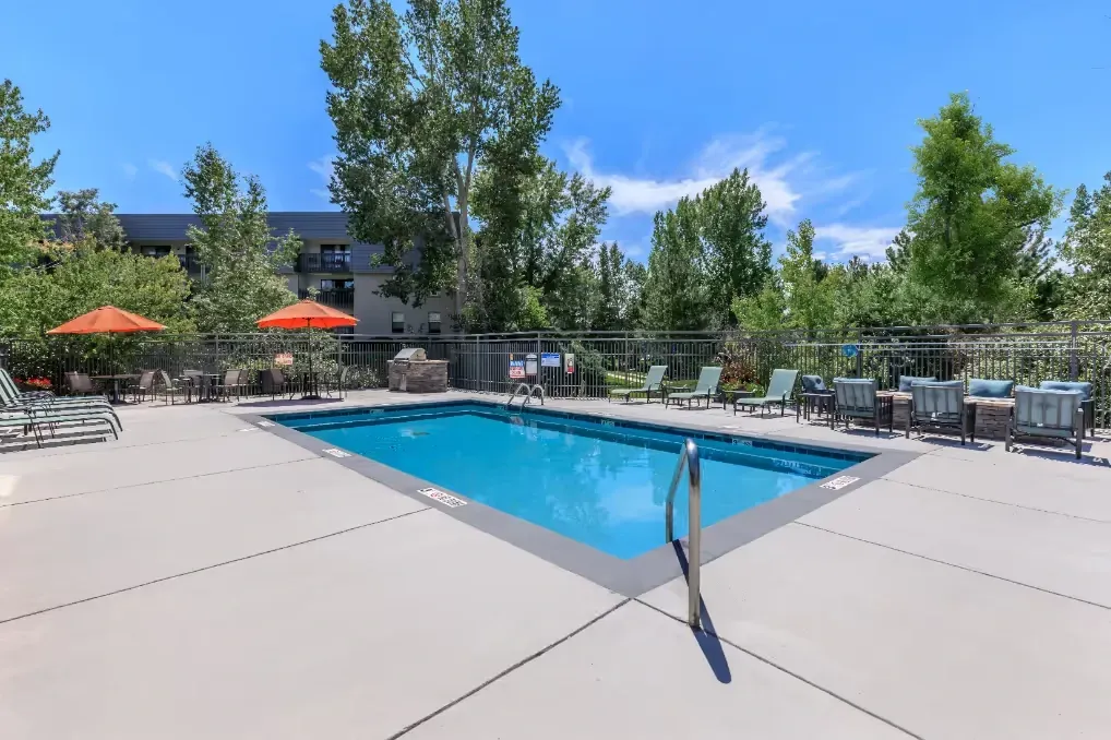 Outdoor swimming pool with lounge chairs, tables, umbrellas, and a grill.