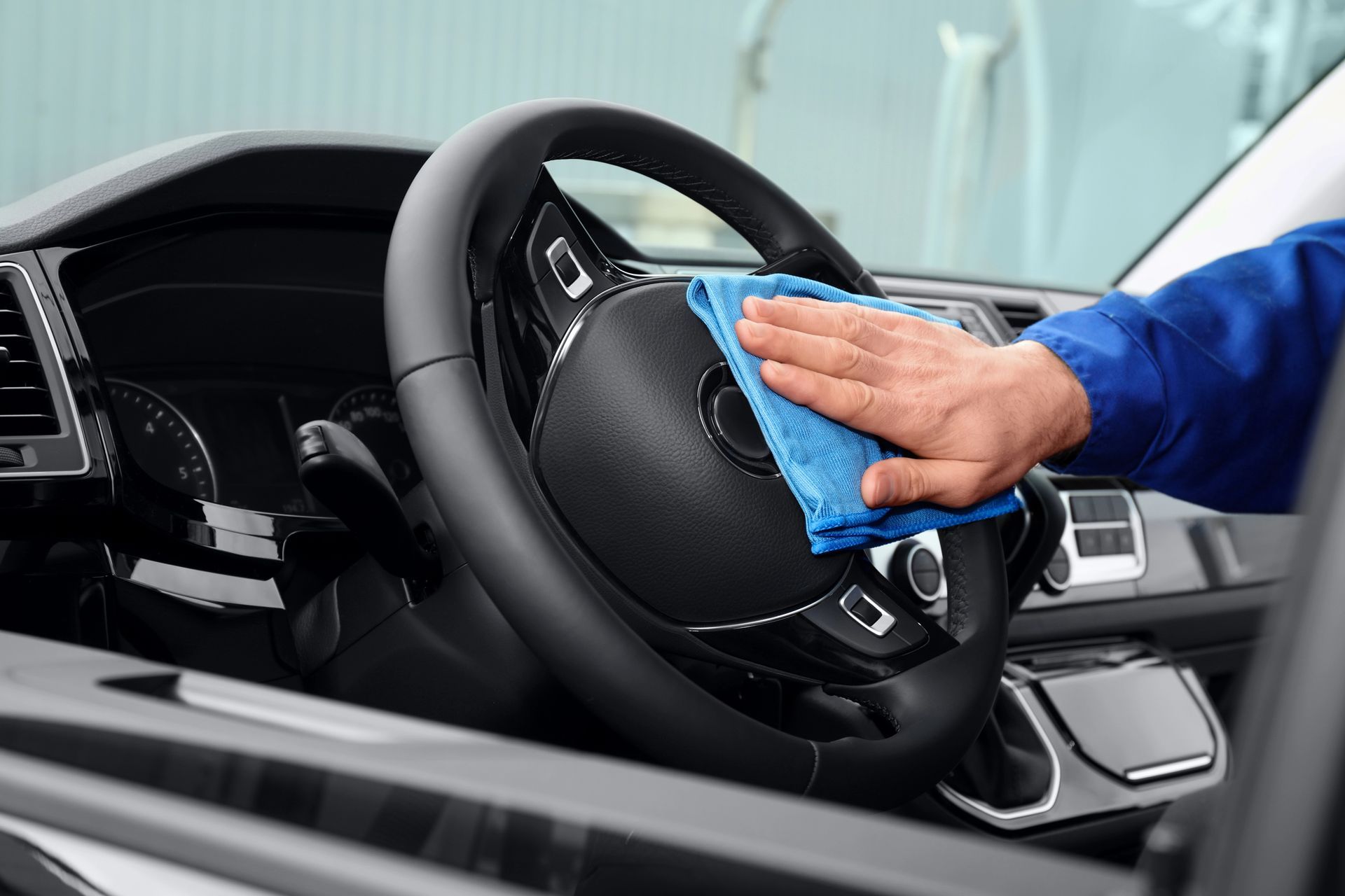 Pulizia manuale del volante di un'auto nera con un panno blu.