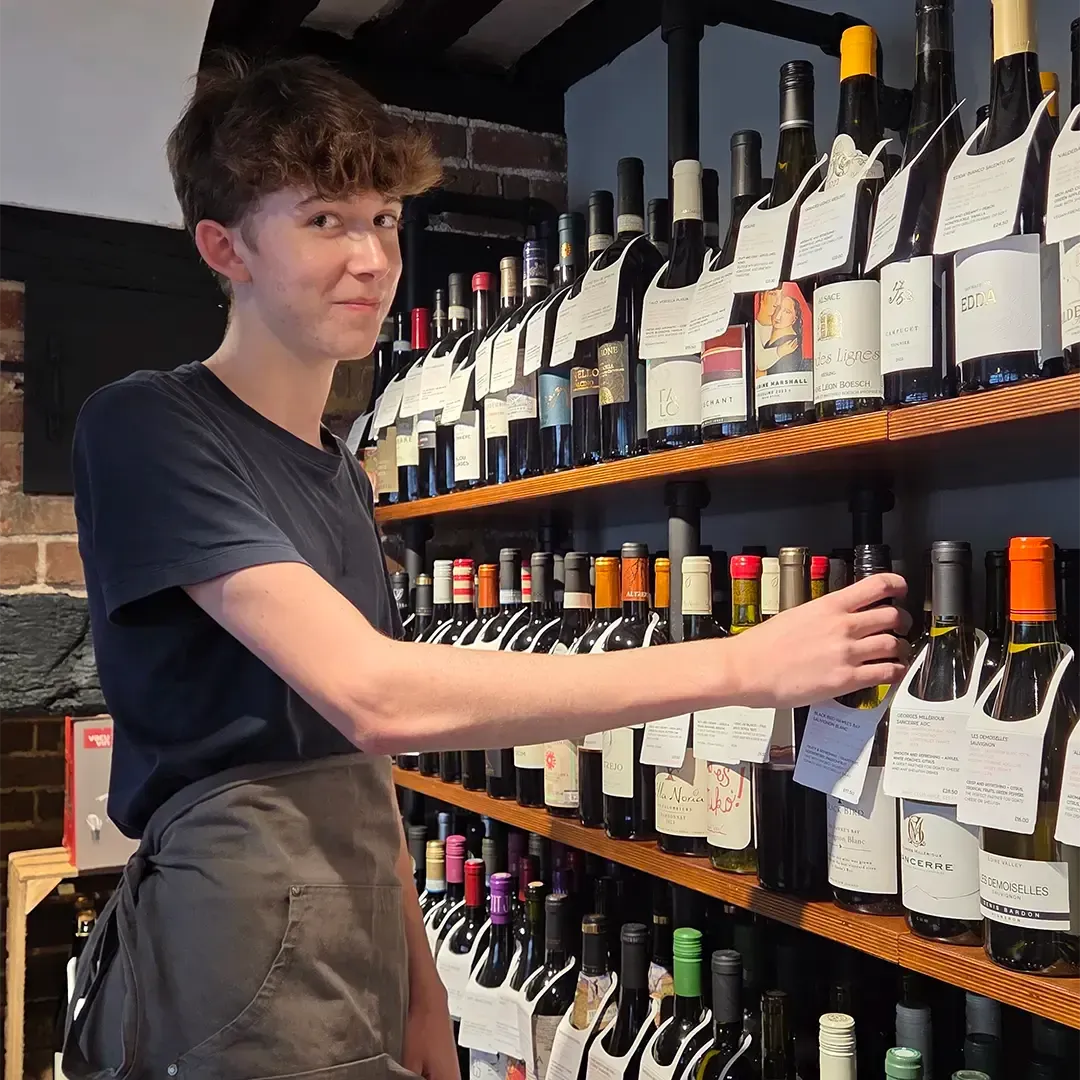 Cameron places a bottle of wine on the shelf at French & Day Delicatessen