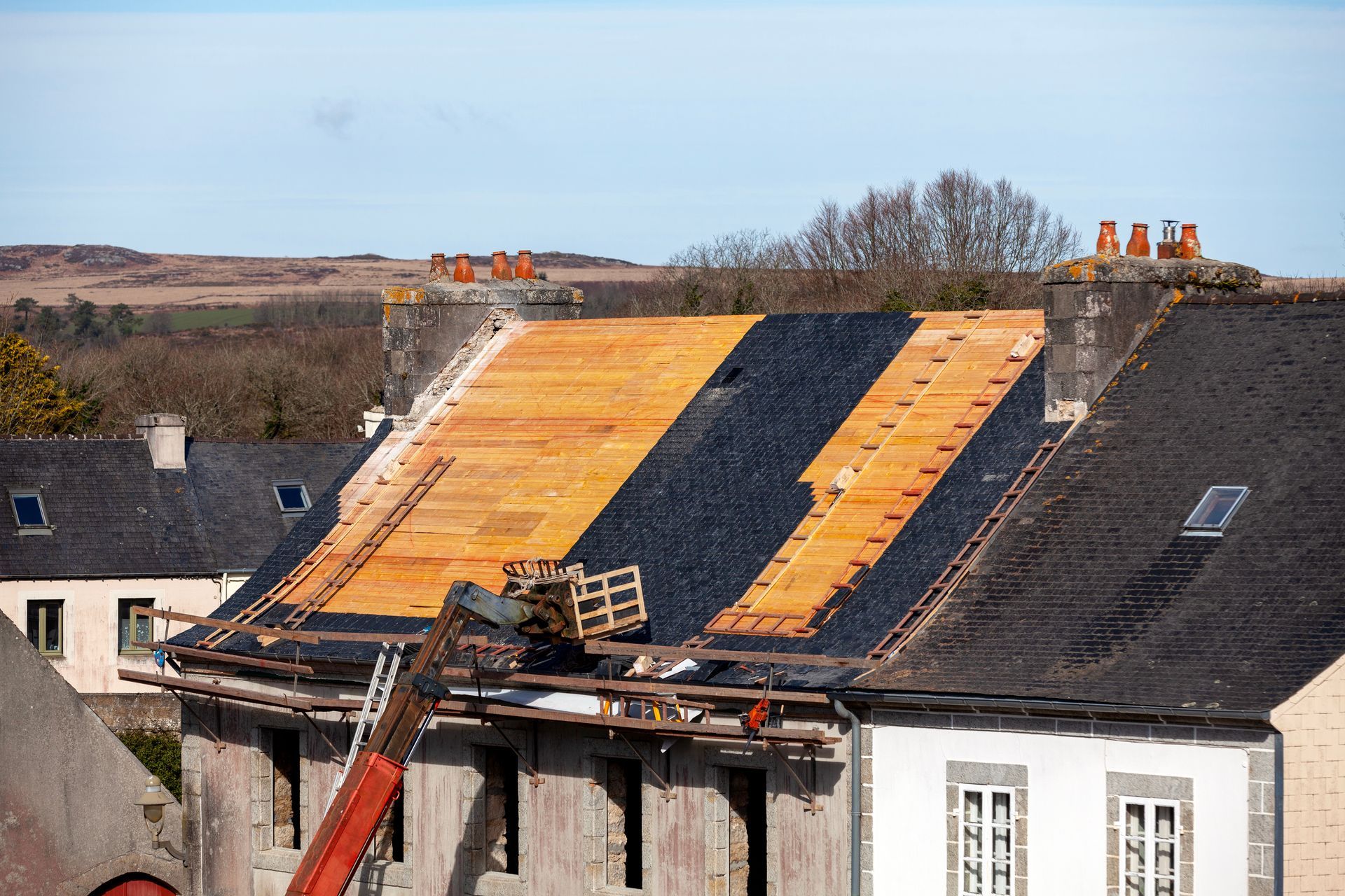 Roof being repaired with orange insulation boards and workers on scaffolding over a row of houses