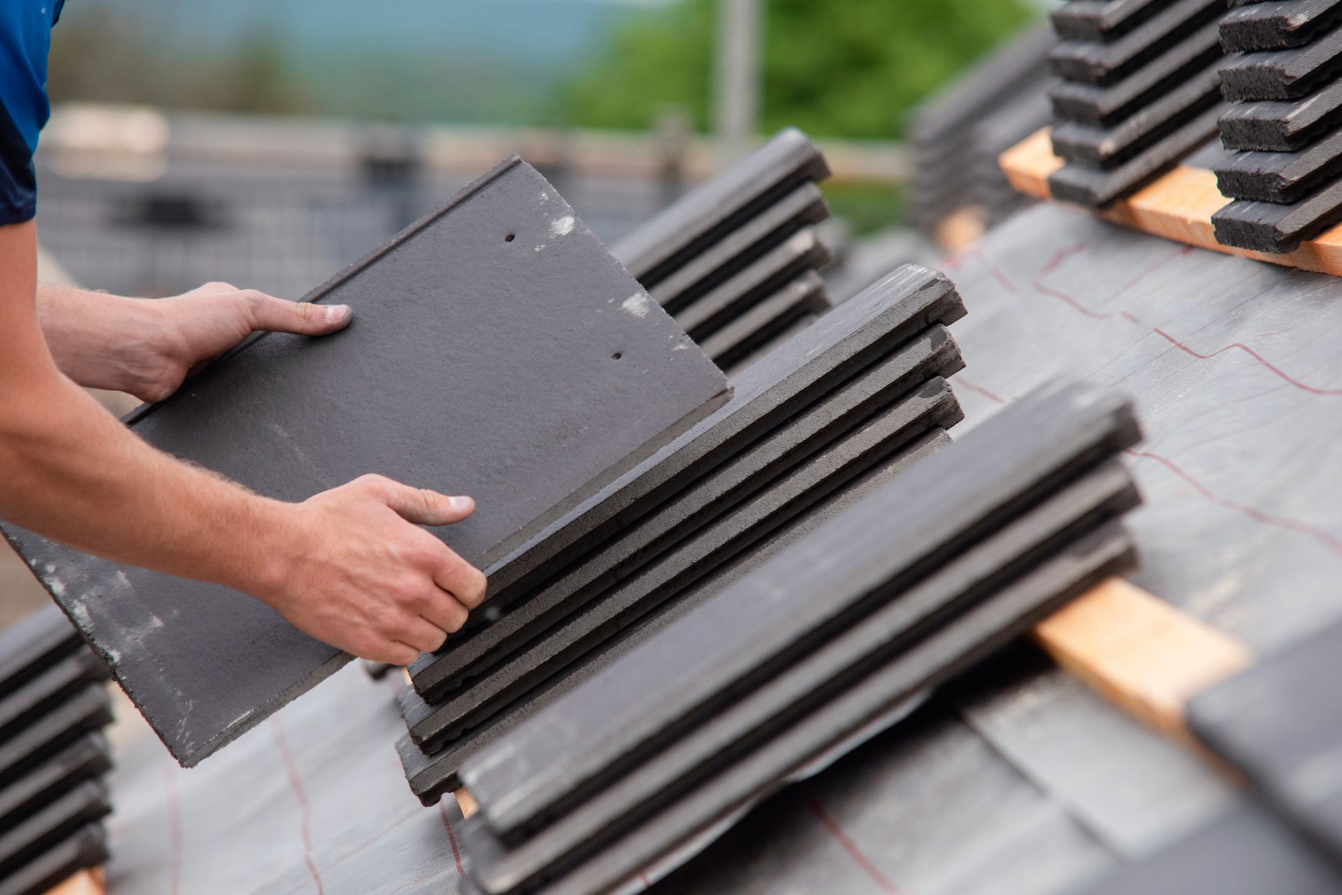 Hands installing dark roof tiles on a sloped rooftop.