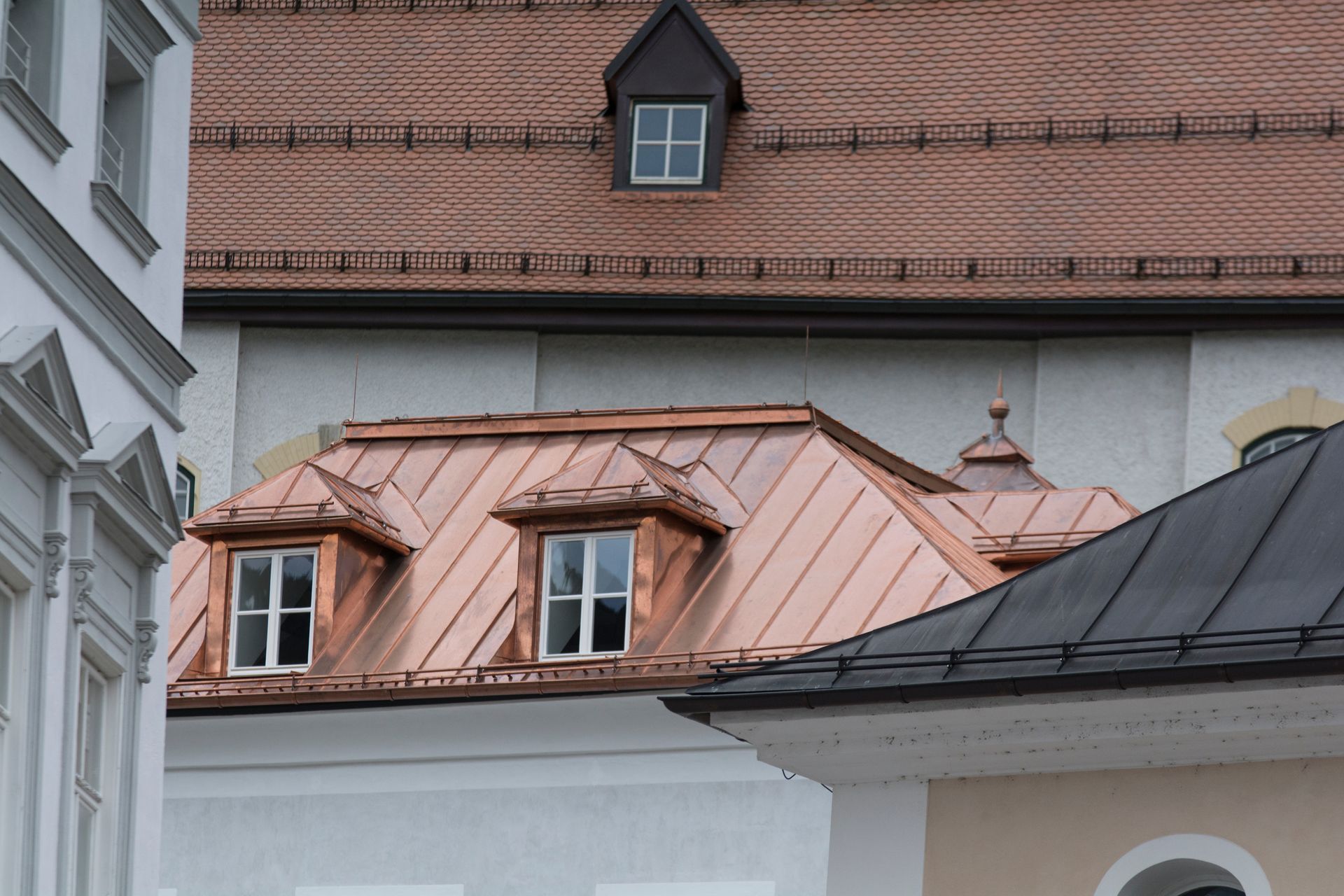 Roofs of European-style buildings with copper dormers and red tiles on an overcast day