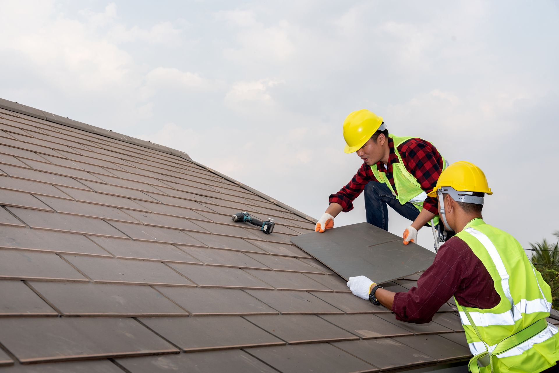 Two roofers in hard hats install shingles on a sloped roof